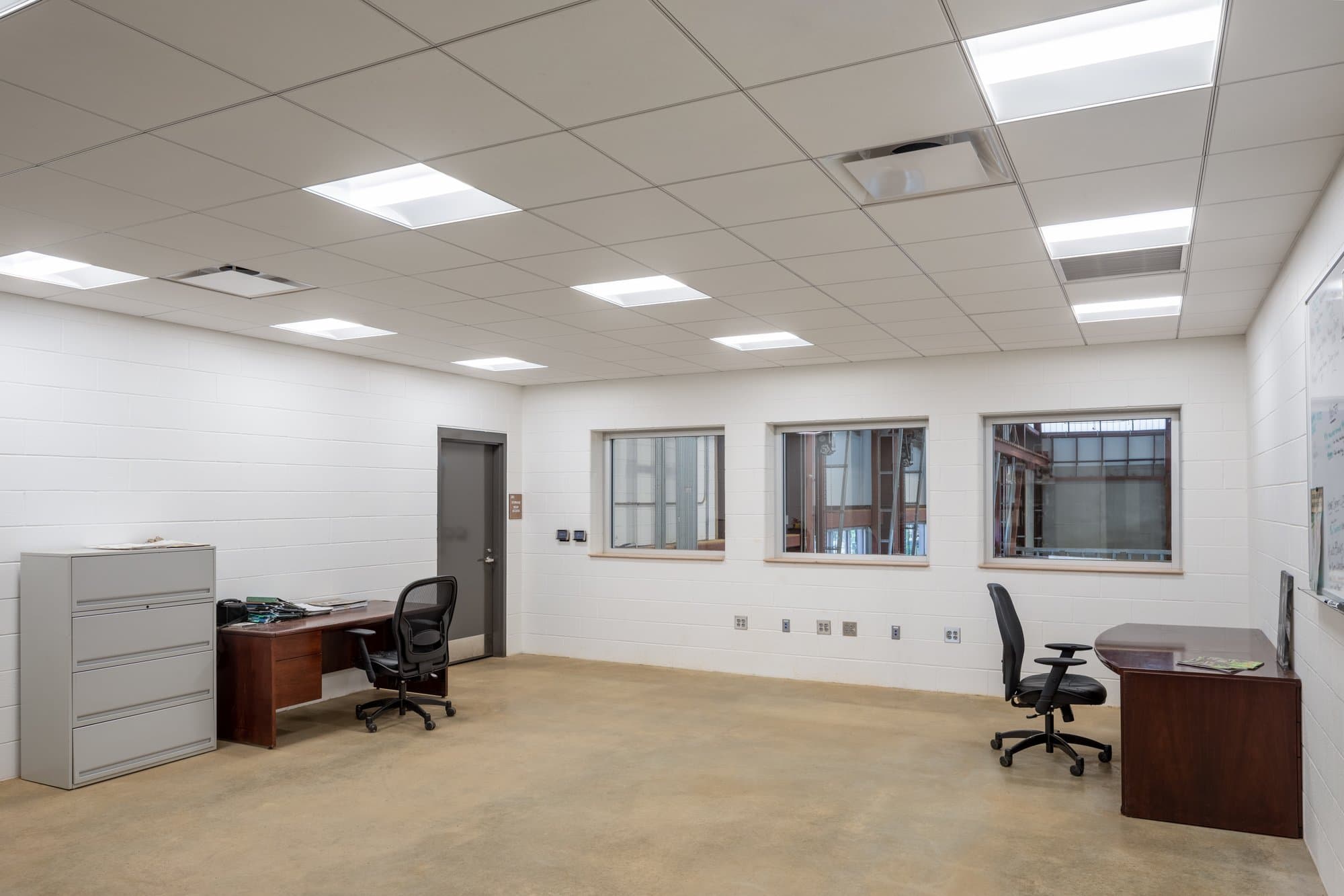 Office space with two desks on either side of the room, a filing cabinet, and 3 windows