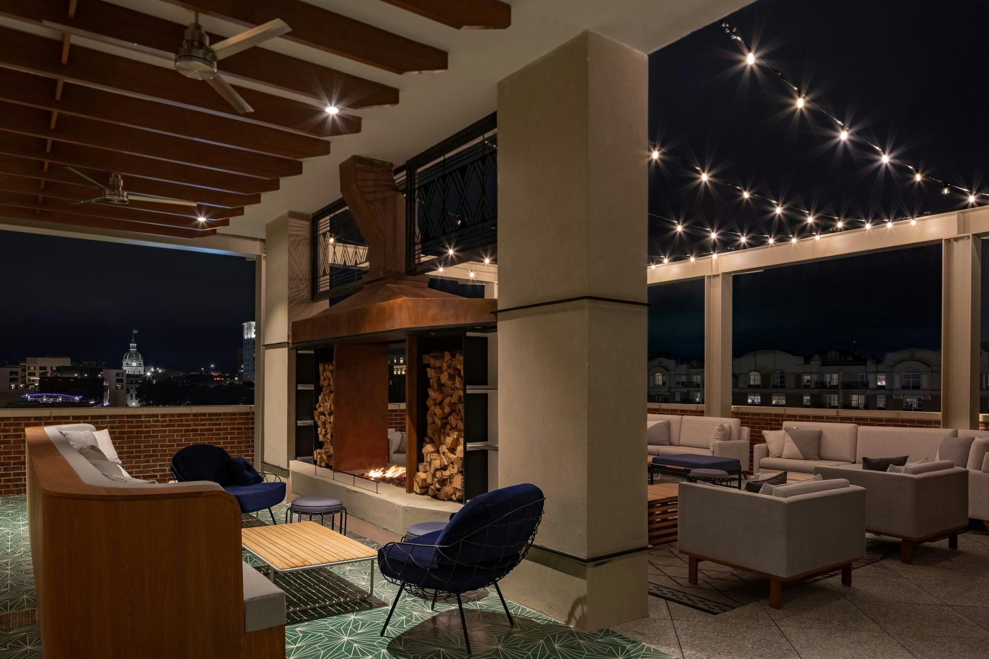 Dimly lit rooftop patio at night with a centrally located fireplace and a variety of couches and chairs.