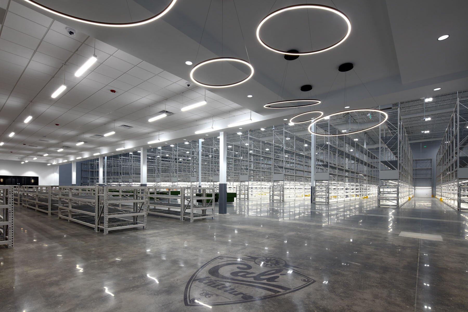 Warehouse showroom with metal display racks, cement floors with emblem and circle light bards hanging overhead.