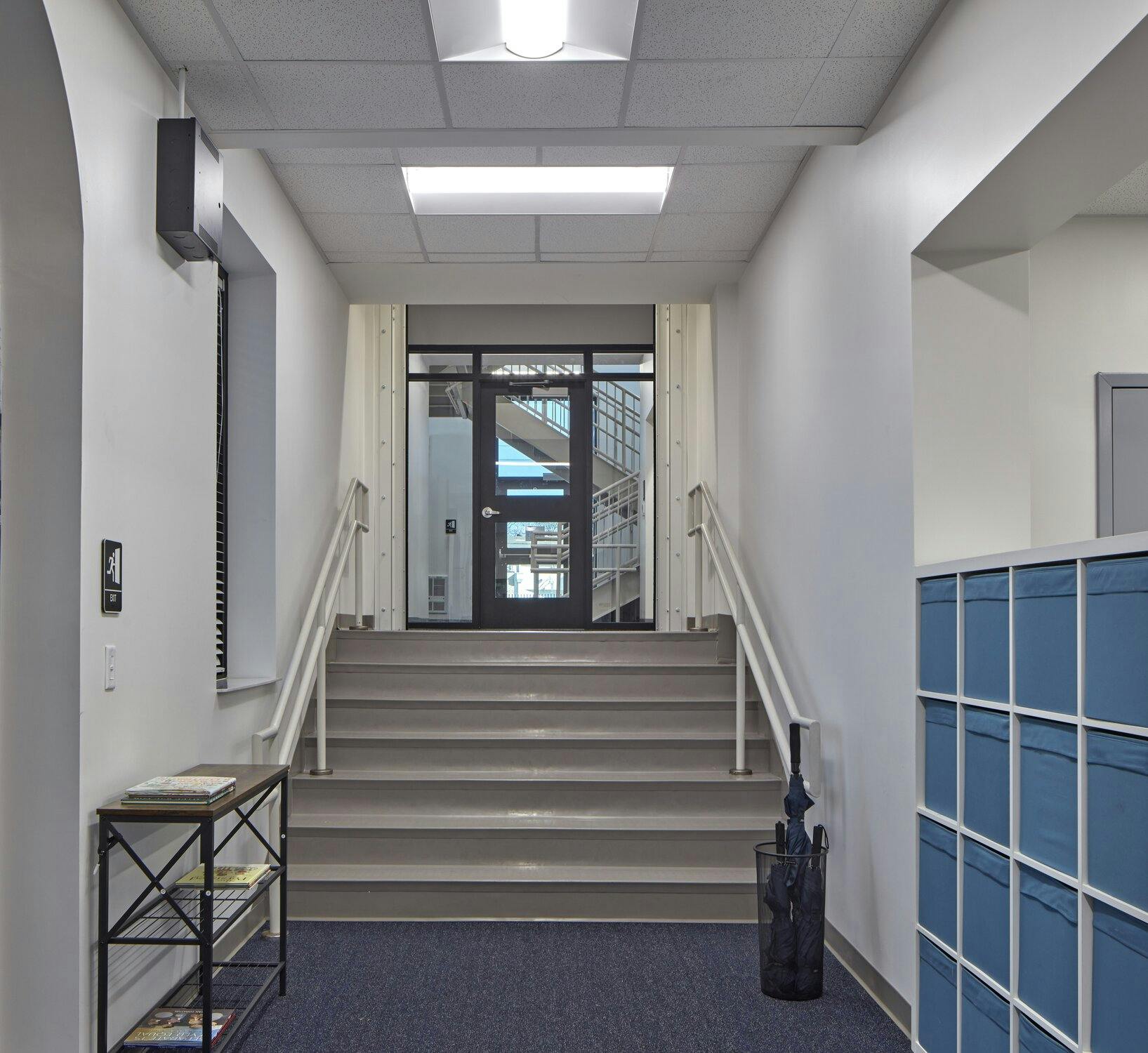 Front entrance of the school with carpeted flooring and a white storage area with blue cubbies leading to stairs and a door