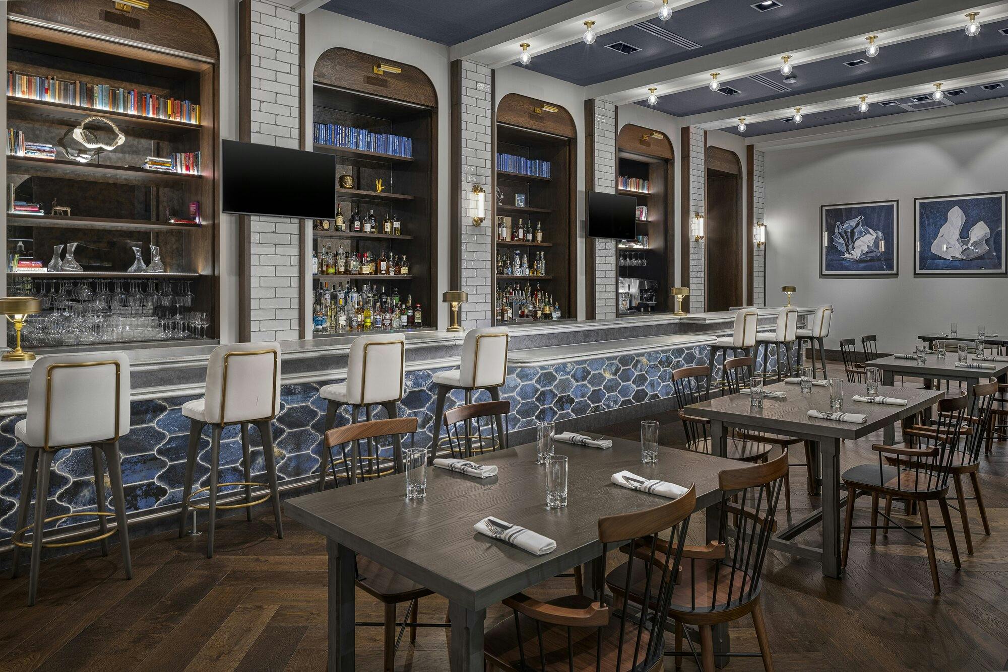 Bar area with track lighting, wood floors, table with chairs and bar stools. Blue tile on bar area matching ceiling color.