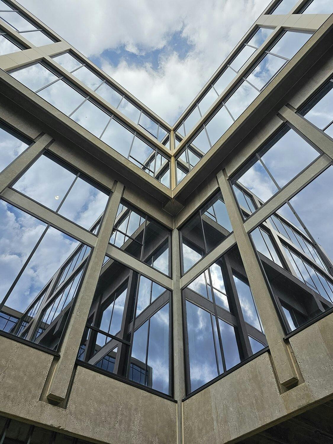 Vertical image of exterior, looking up towards sky surrounded by windows incased in black frames.