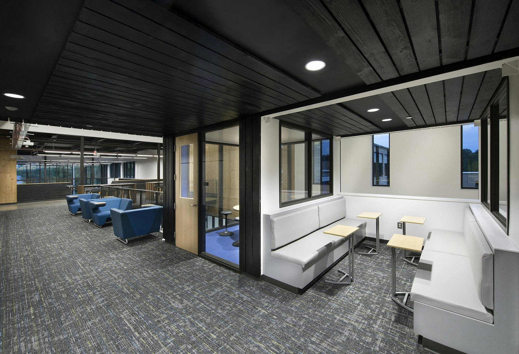 A carpeted room with dark ceilings contains multiple nooks with tables and seating.