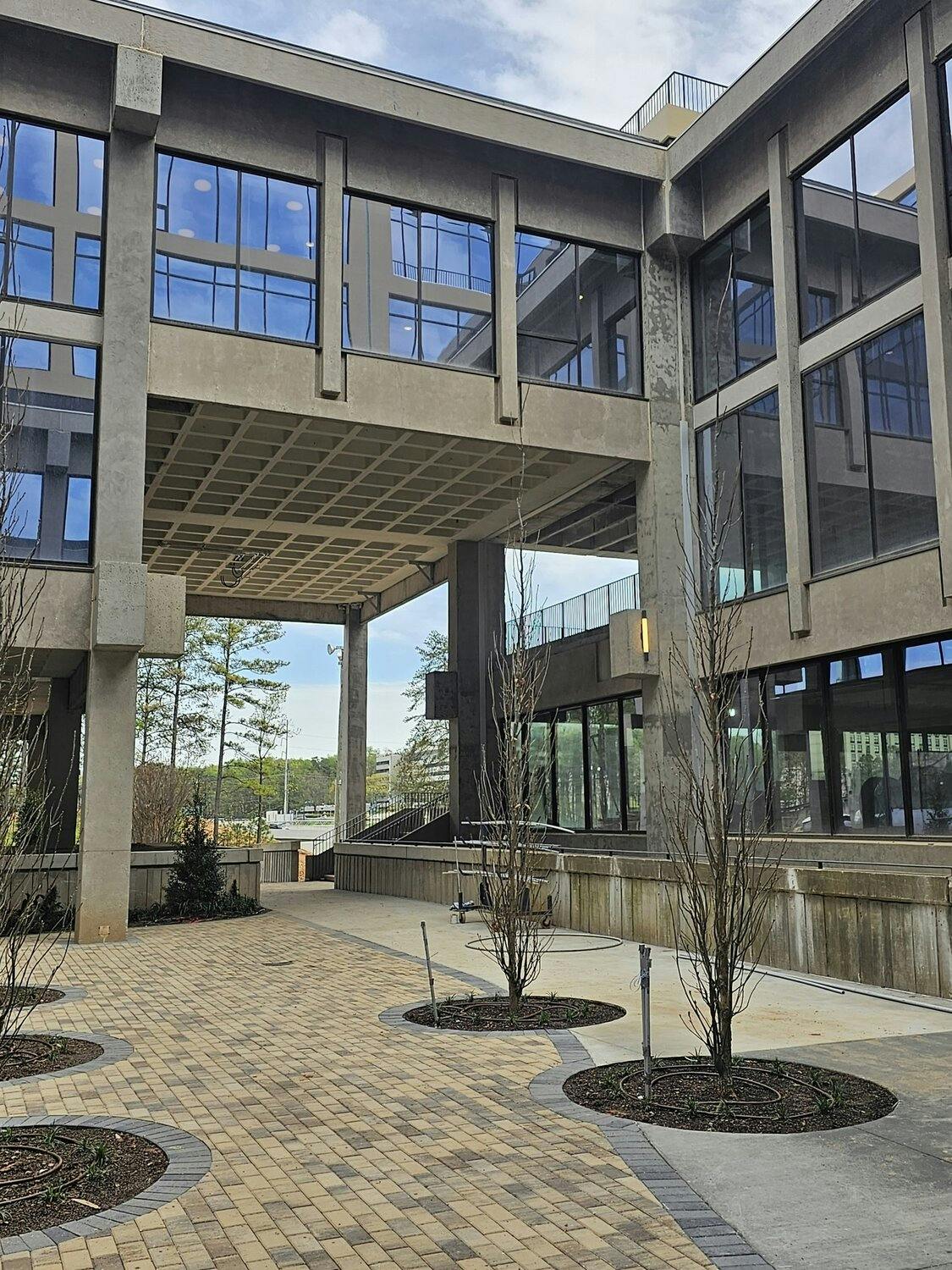 Passage entrance into building with concrete facade, windows, and lanscaping with trees and shribs.