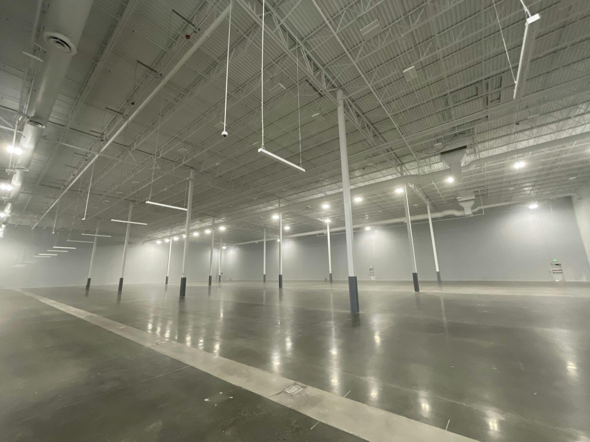 Interior image of warehouse with poured concrete flooring, exposed beams ceiling and lighting.