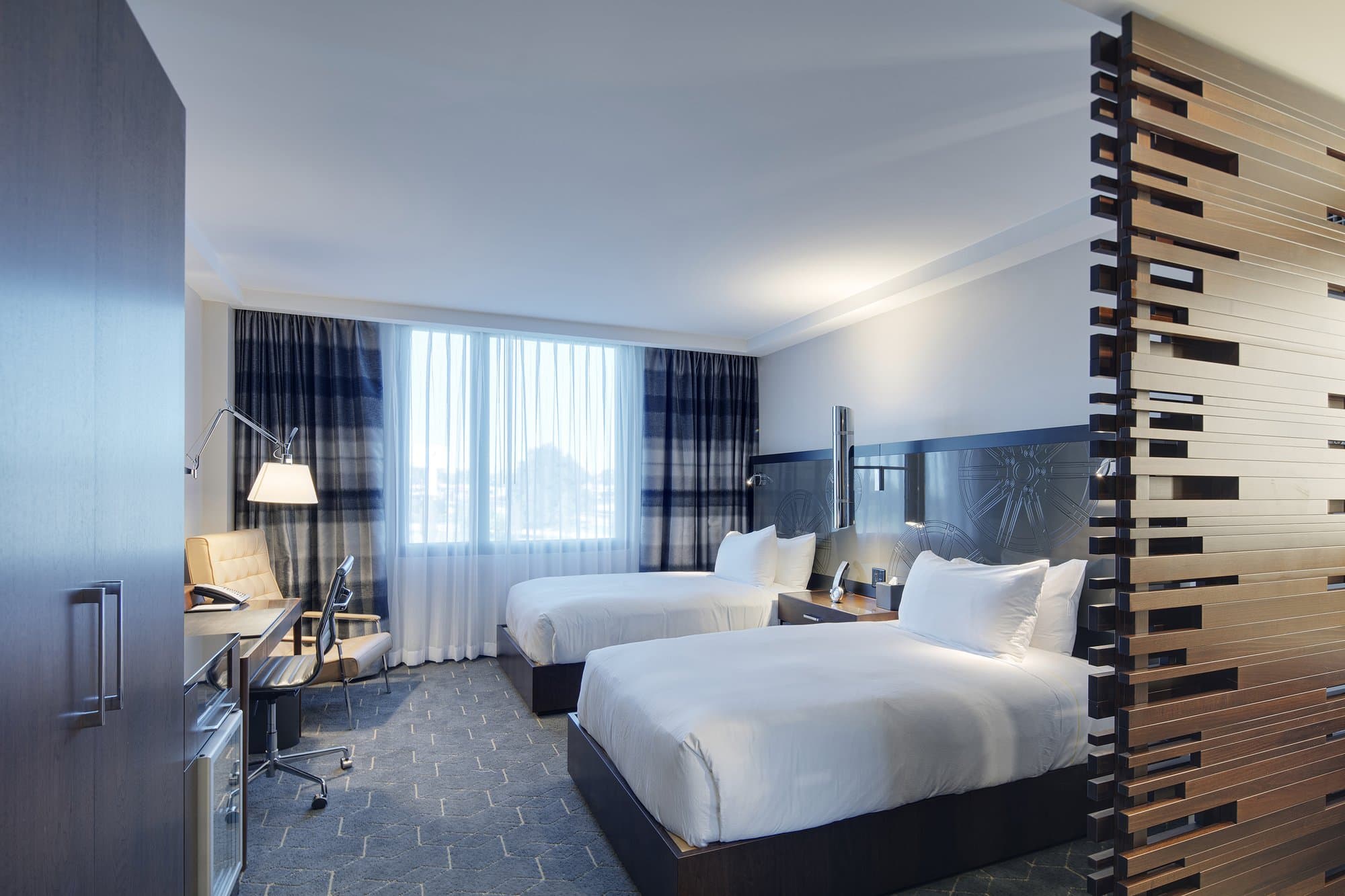 Modern hotel room with two double beds and a unique wood trimmed half-wall separating the bedroom from another space.