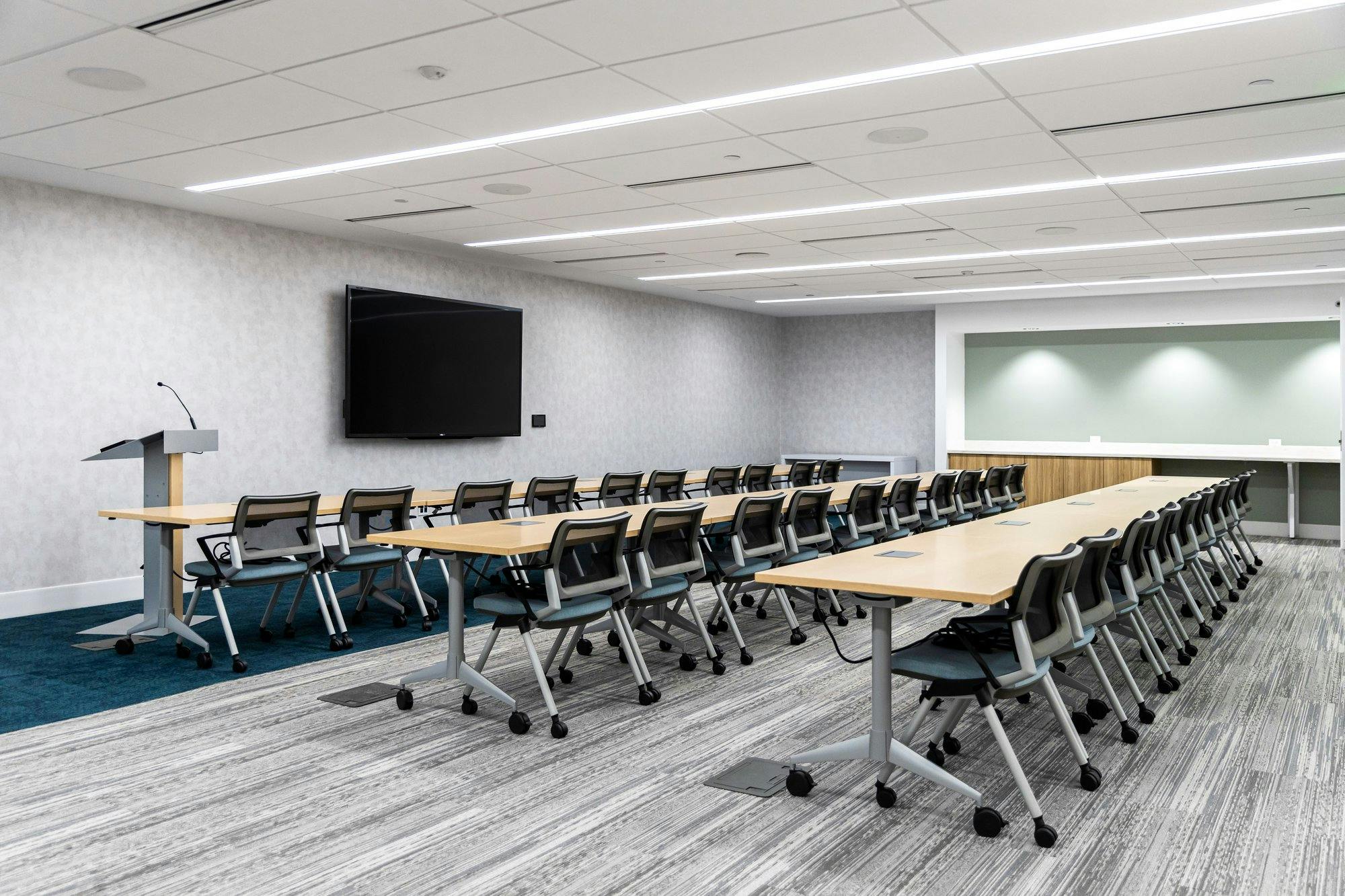 large conference room with three rows of tables facing the front of the room, where there is a lectern and a television screen which can be used for presentations