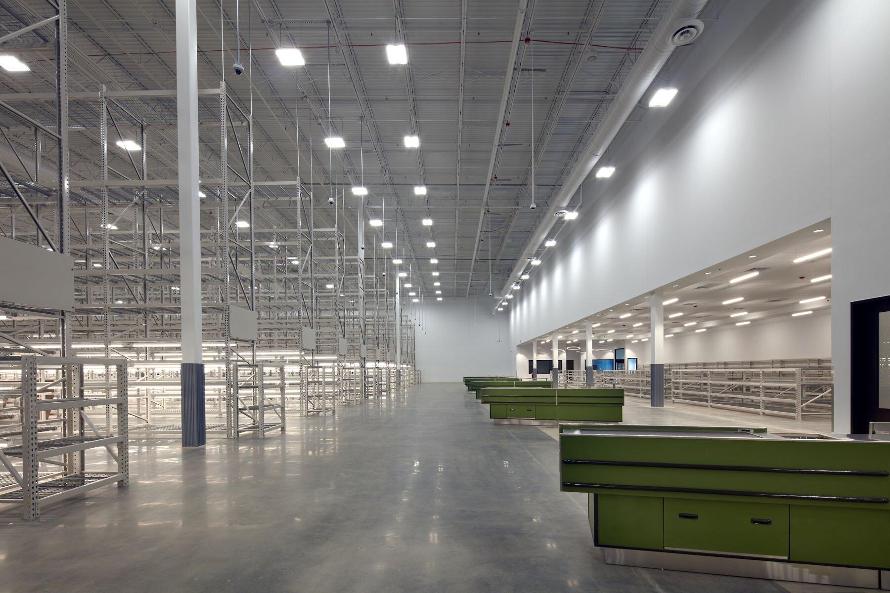 Warehouse view with tables, metal racks, cement floors, and hanging lights.