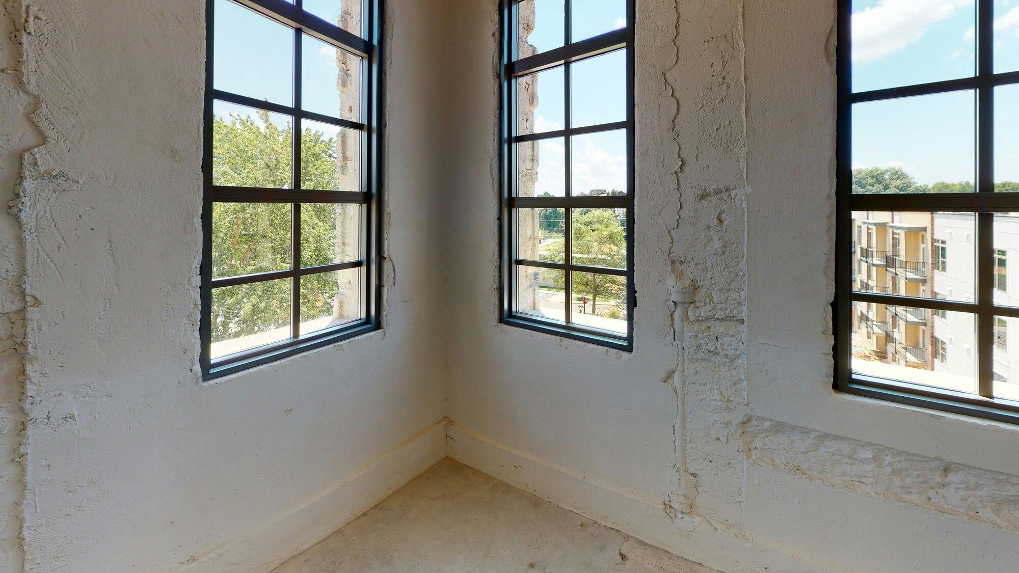 A corner of a white room with black framed windows on each side of the corner.