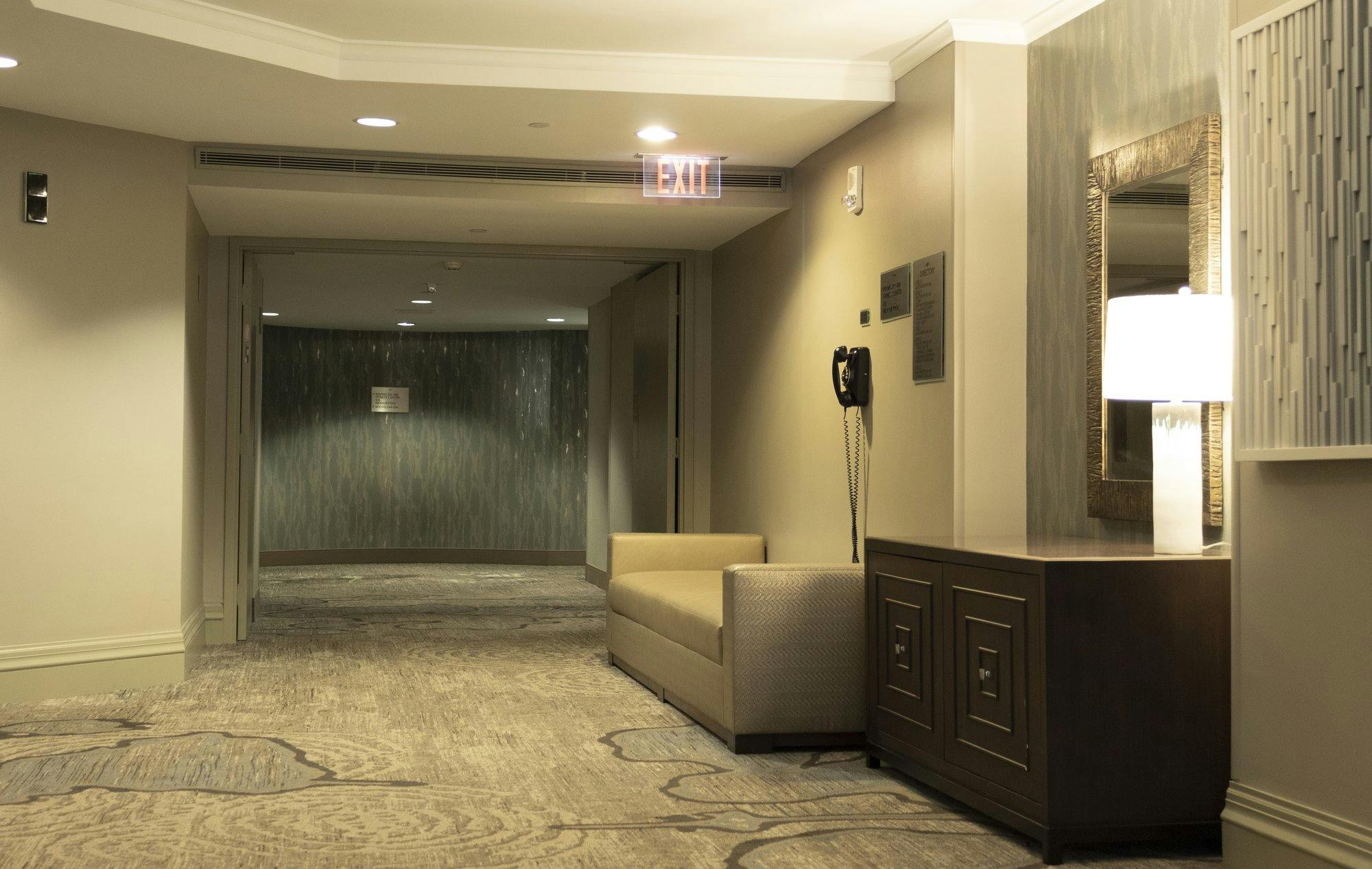 Elevator lobby with bench, phone, mirror, and exit sign.