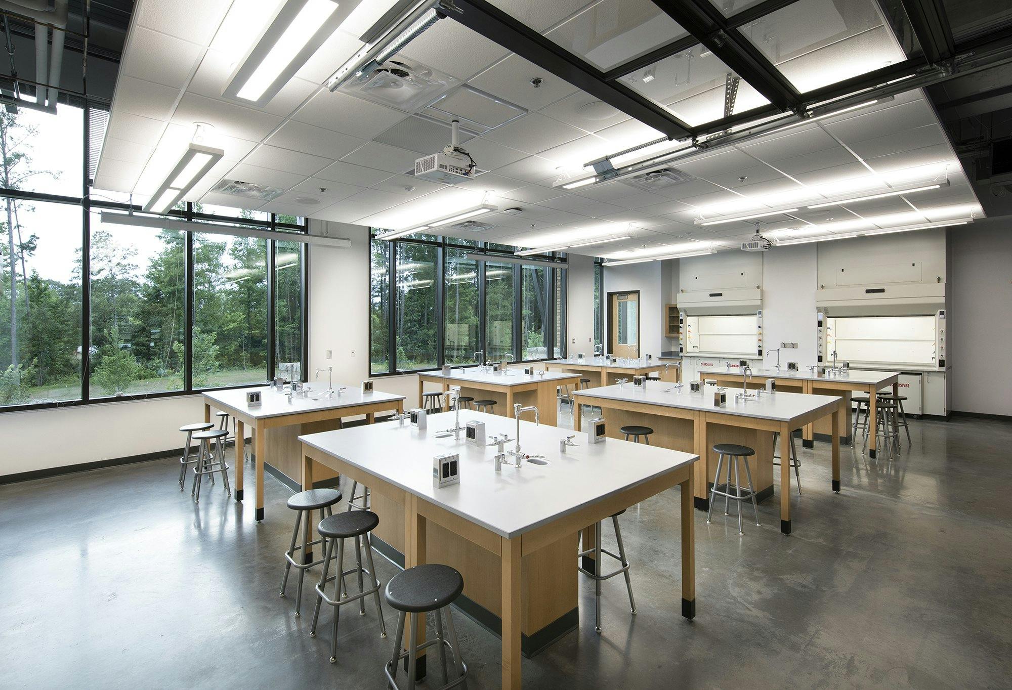 A science lab with large windows illuminate a room with multiple scientific workstations containing barstools for seating.