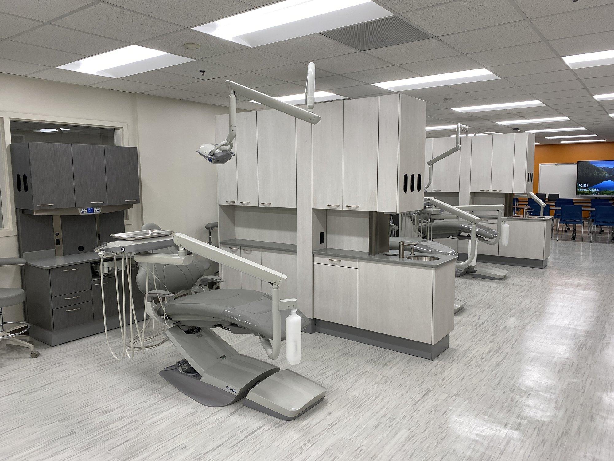 A dental clinic setup with white cabinets, patient chair, and an overhanging light.