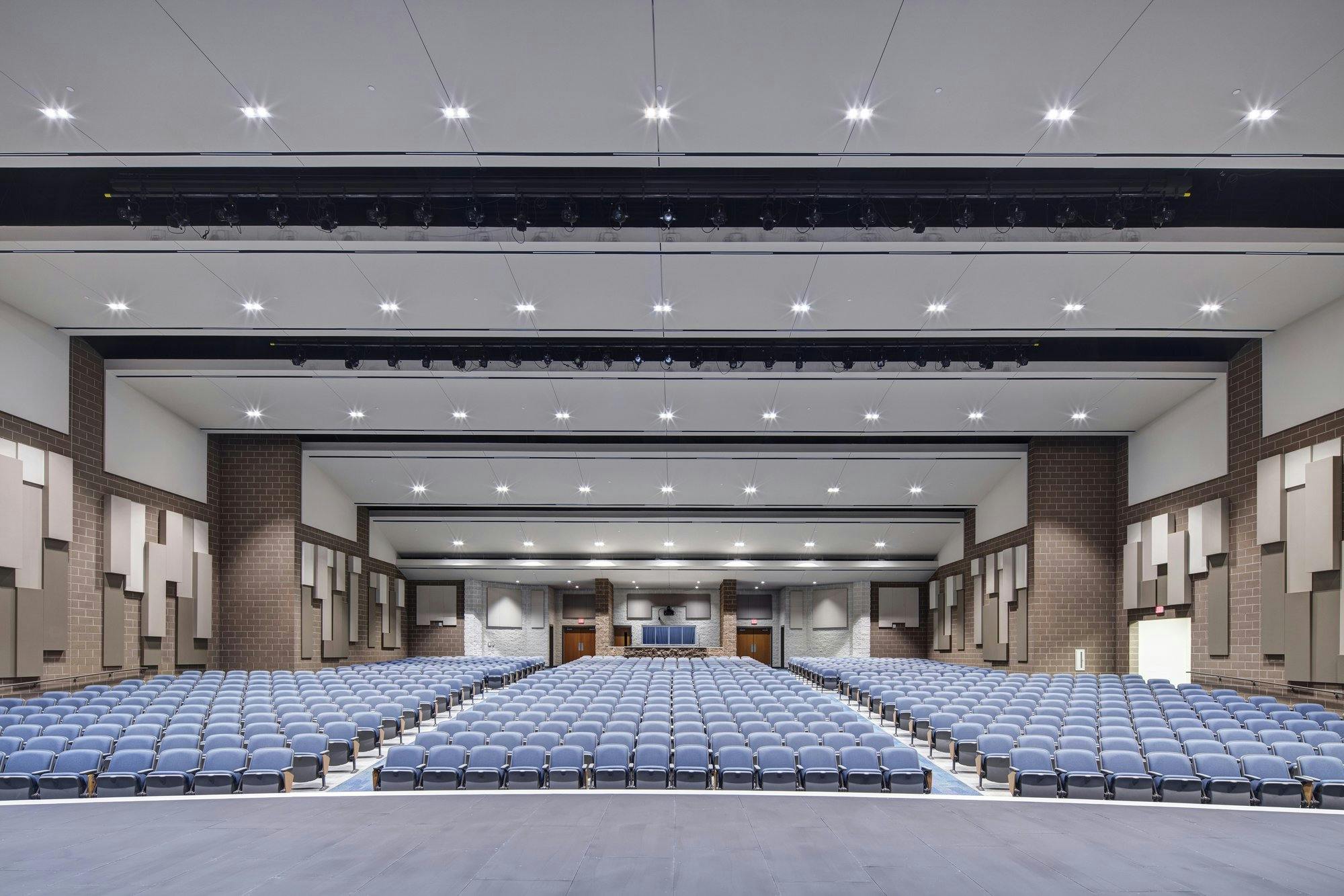 Rows of blue chairs seen from the stage of a wide open high school auditorium.