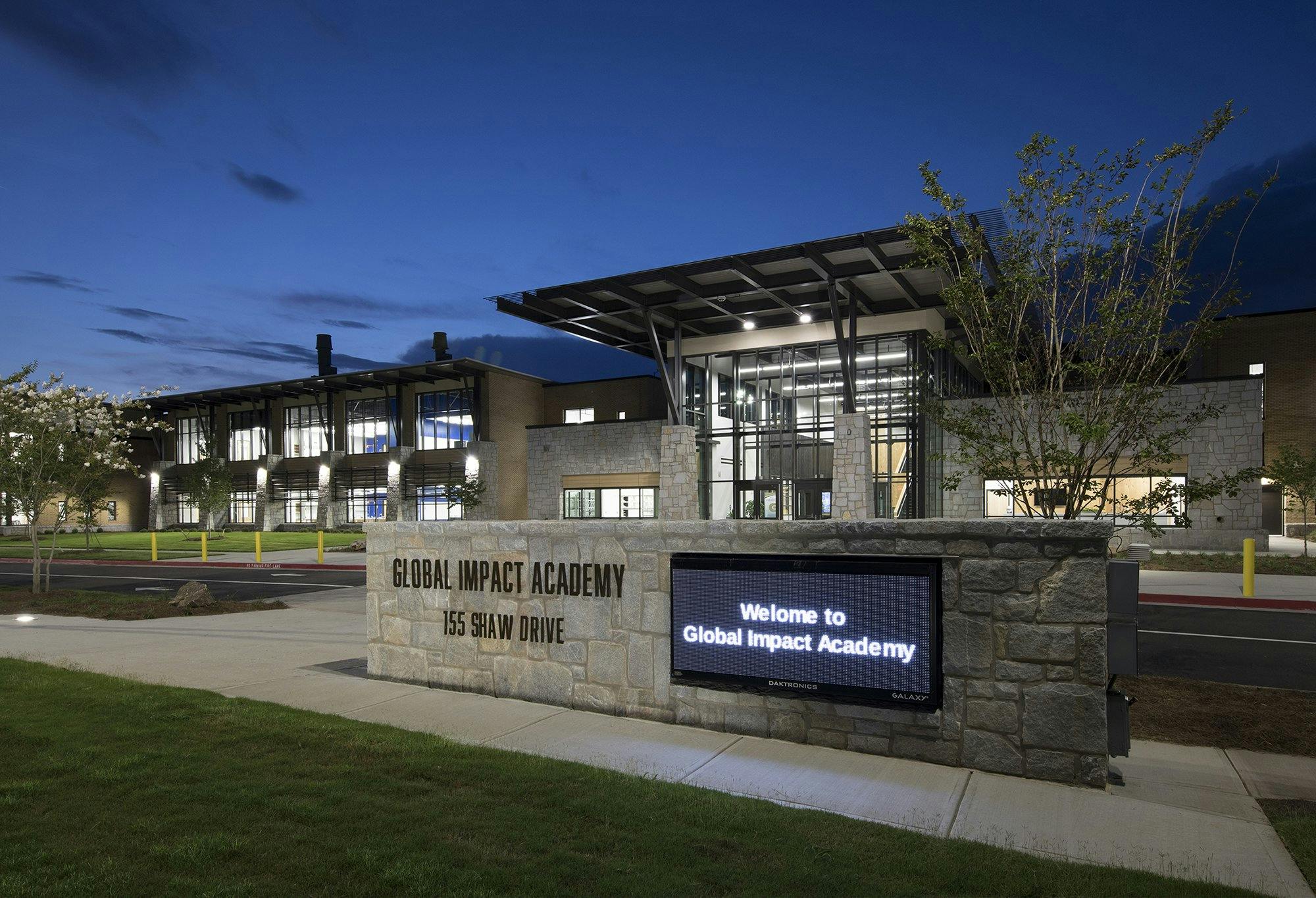 Light is seen coming from the windows of the Global Impact Academy building at dusk.