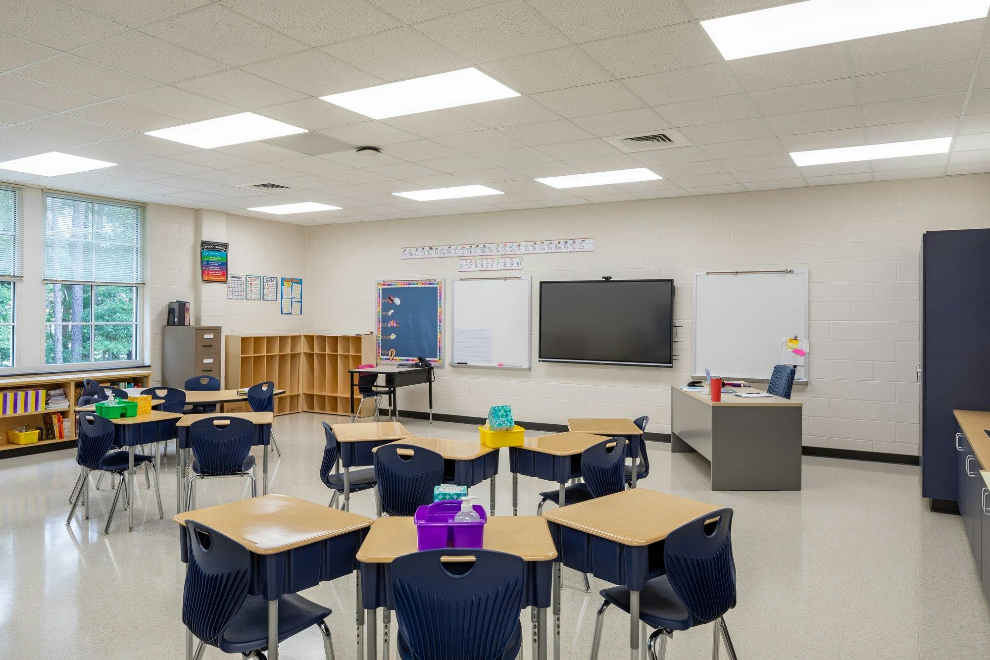 Desks are clumped together throughout a well-lit elementary school classroom.