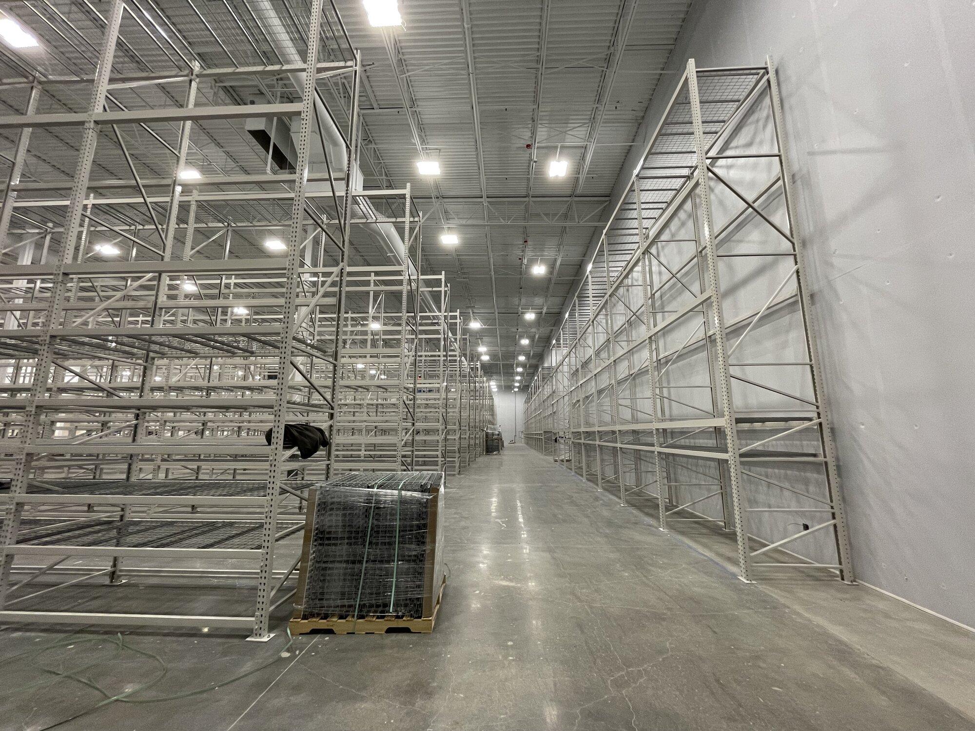 Interior image of warehouse with poured concrete floors, shelving and overhead lighting.