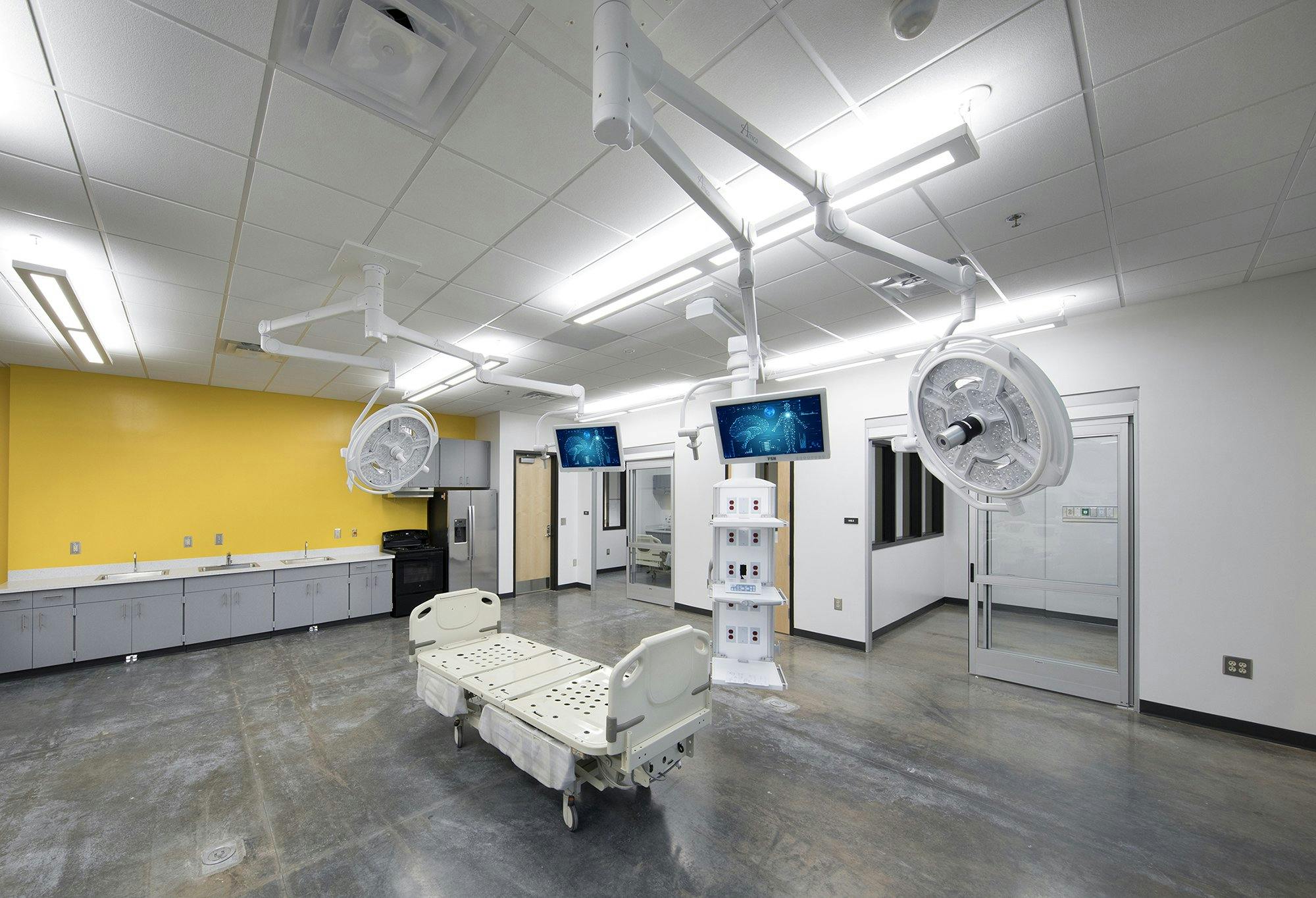 A medical education room with a hospital bed and multiple overhanging lights and screens. 