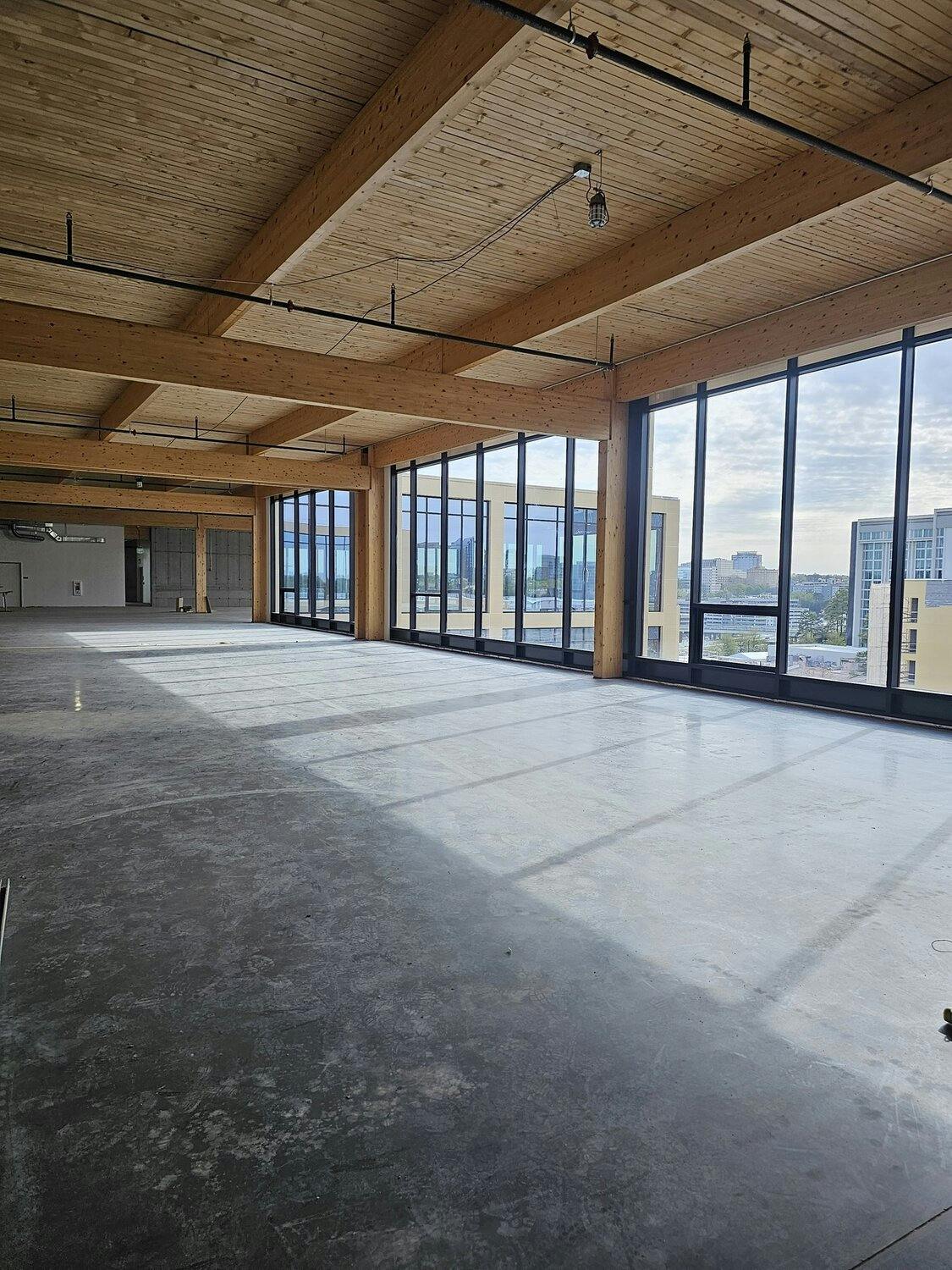 Interior with concrete floors, timber beams on walls and ceiling with windows incased in black frames, overlooking city.