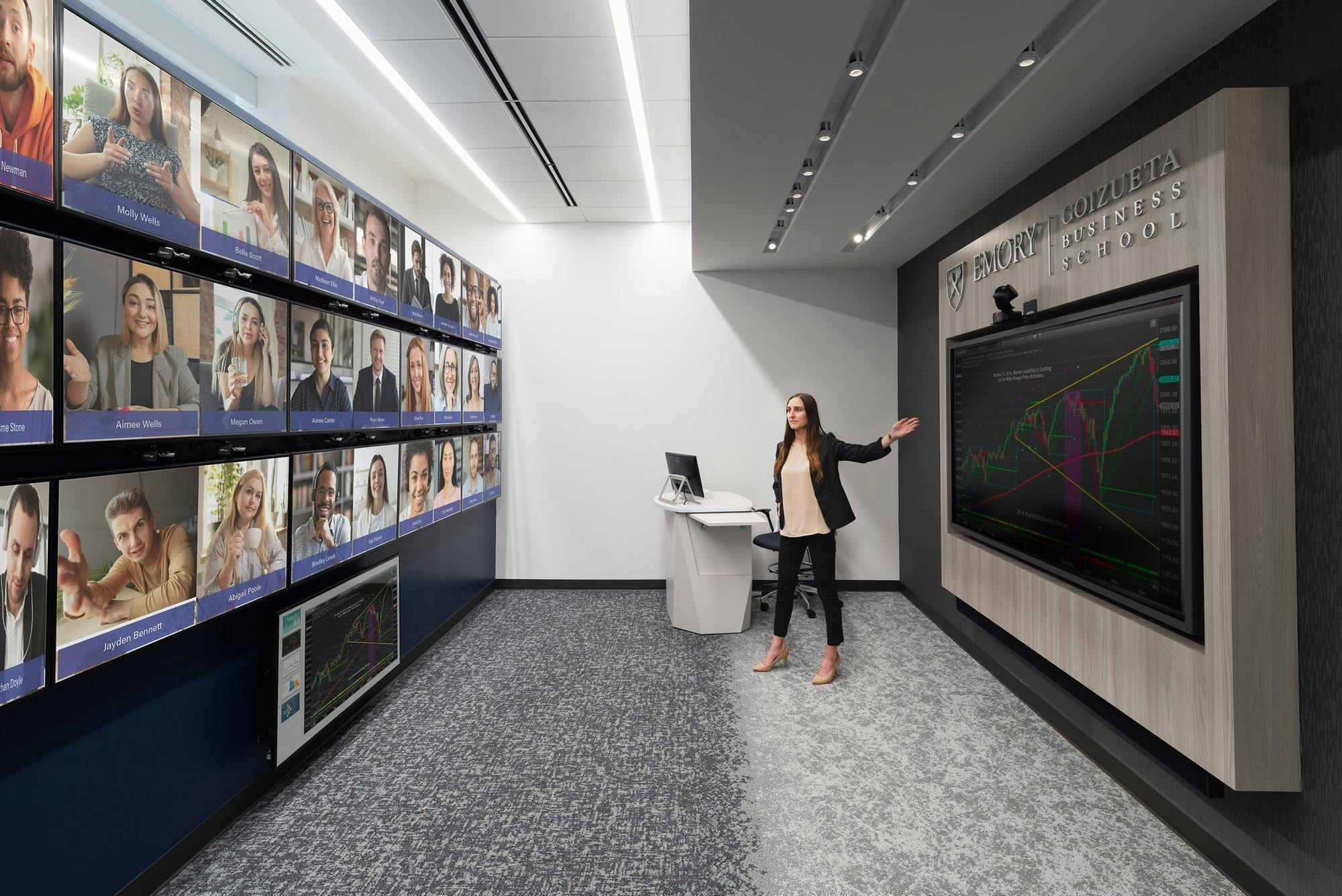 Woman presenting to a wall of virtual attending students in front of a presentation screen.