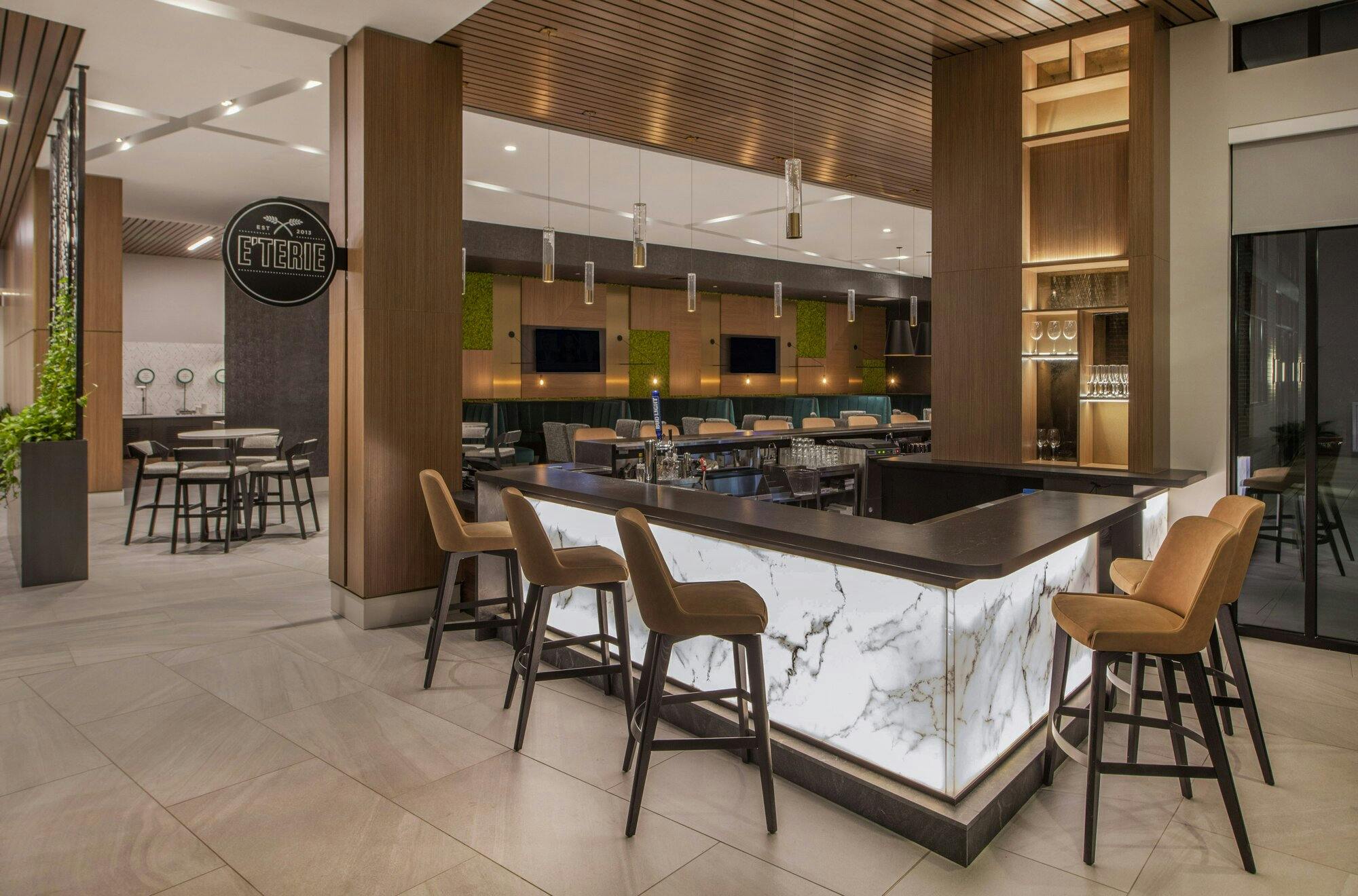 Bar area with lighted stone underneath, with leather stools, and a wood beam ceiling above bar.