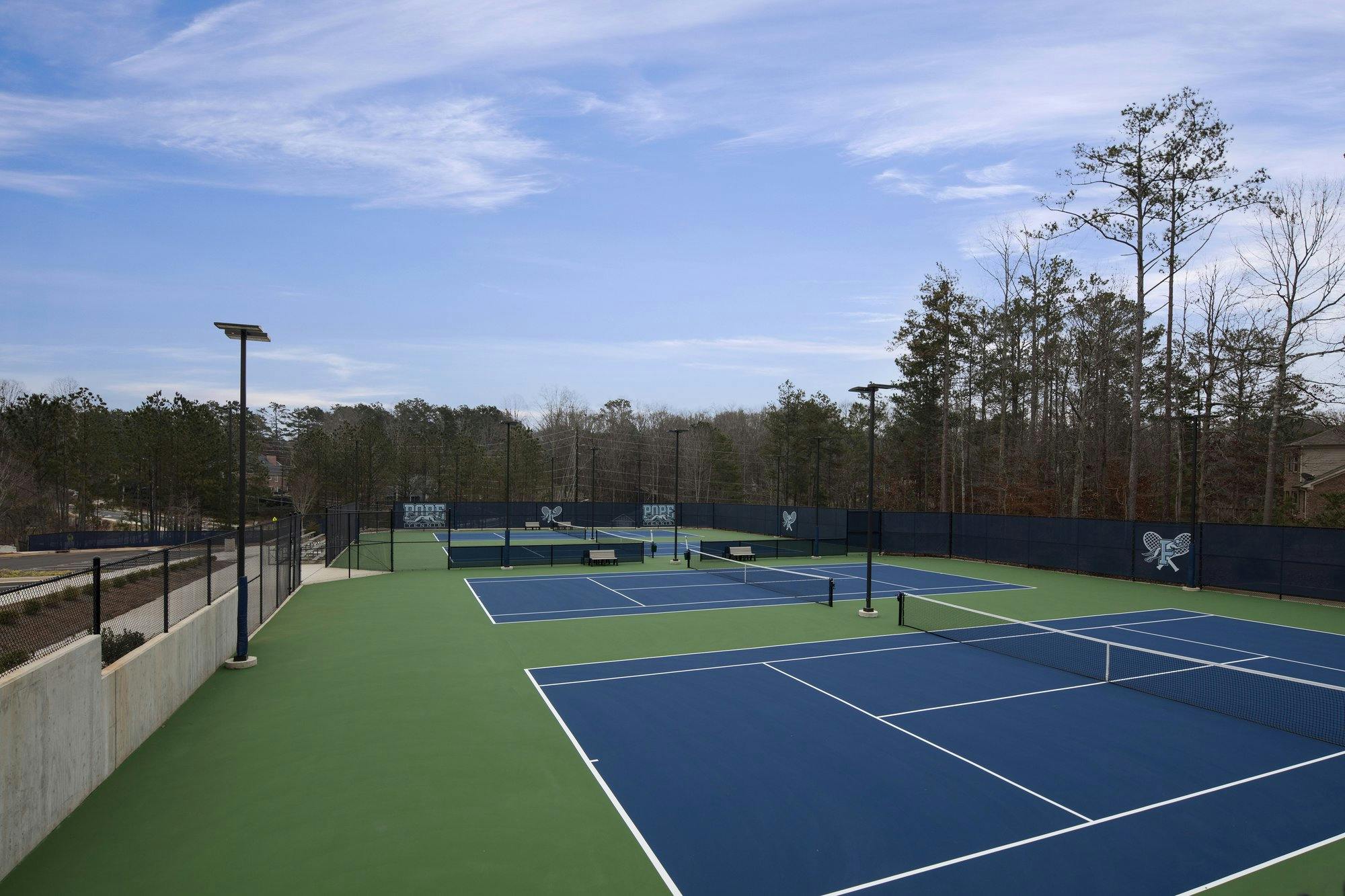 Multiple tennis courts lined up on a blue-sky day at Pope High School.