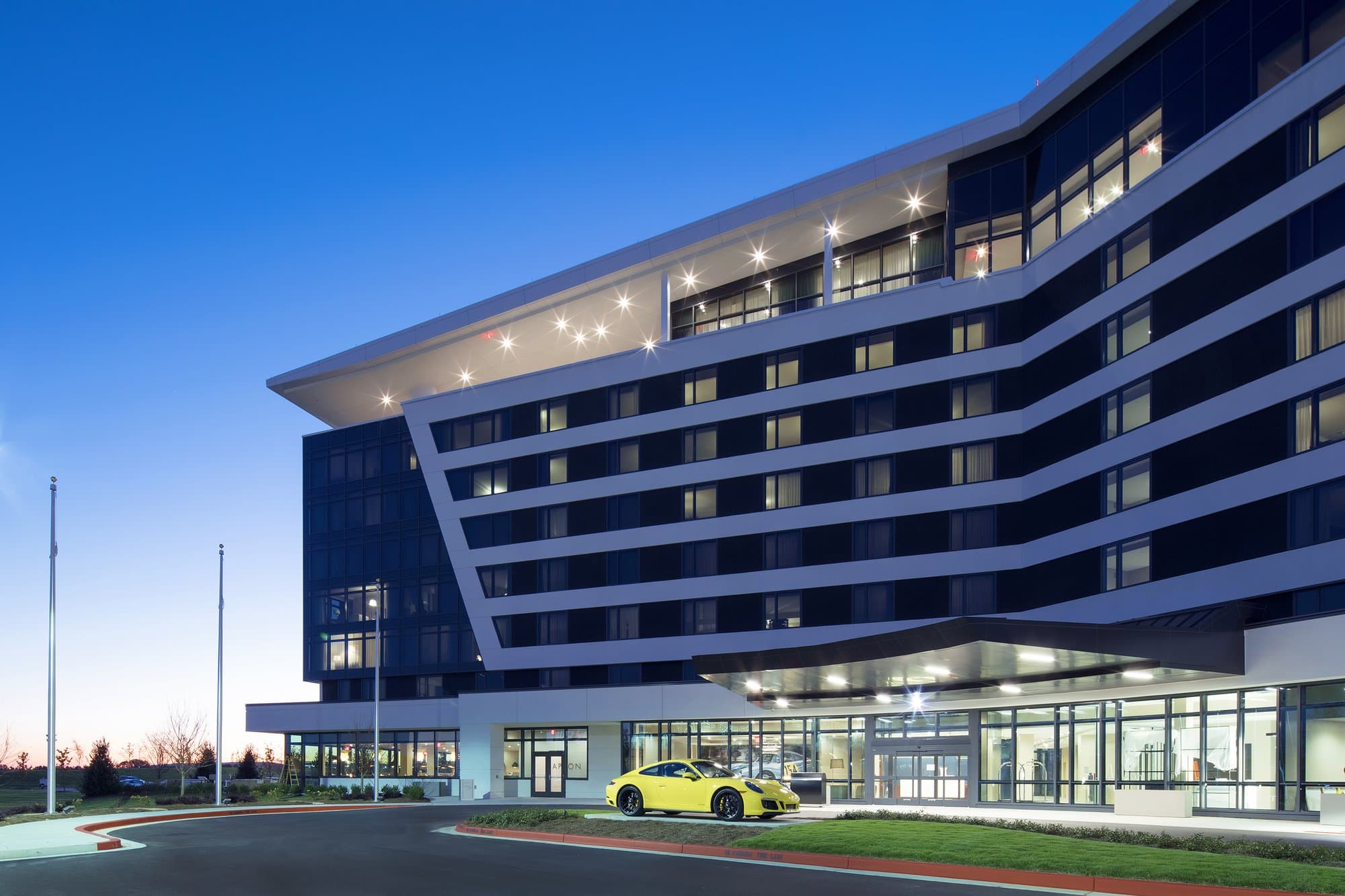 Modern building with rows of white accents surrounding dark windows. Lights dot the top floor at dusk.