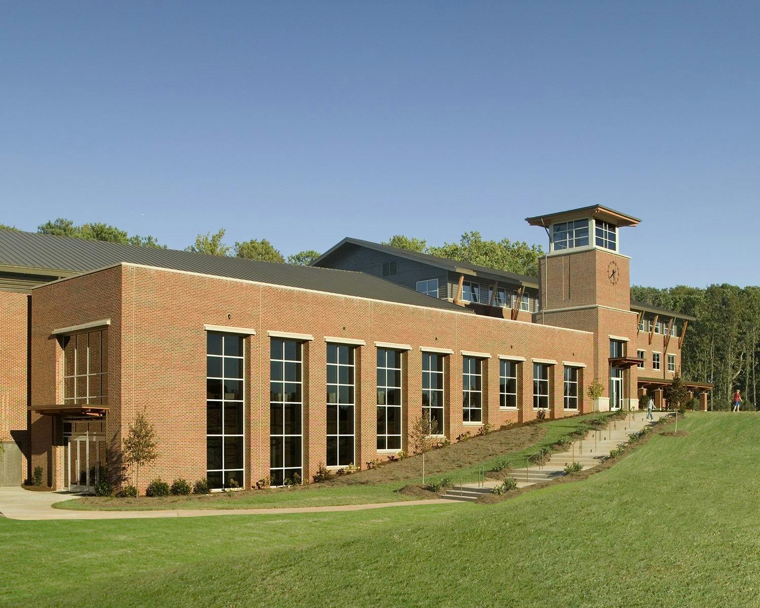 Stairs on a grassy hill lead to the entrance of a brick structure school featuring a clock tower.