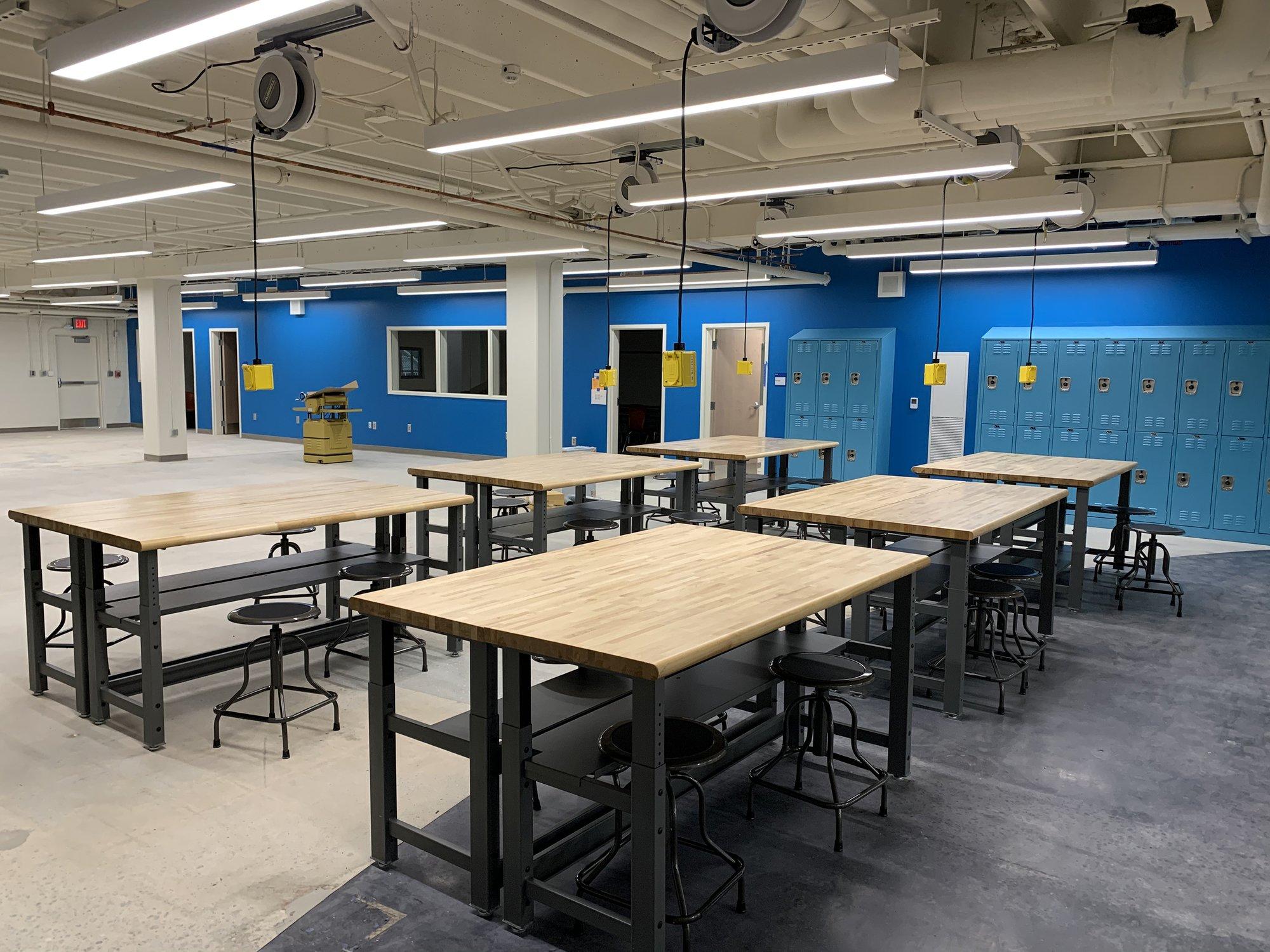 A series of wooden tables and stools are lined up in a large room with painted blue walls.