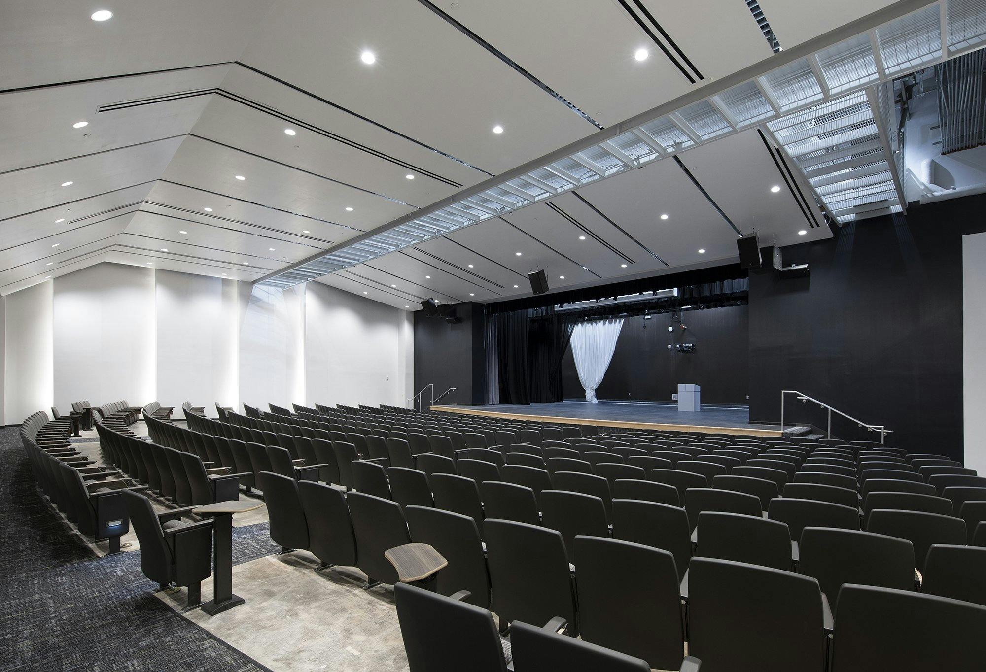 Large auditorium with many rows of seats all angled toward a stage in the back of the room.