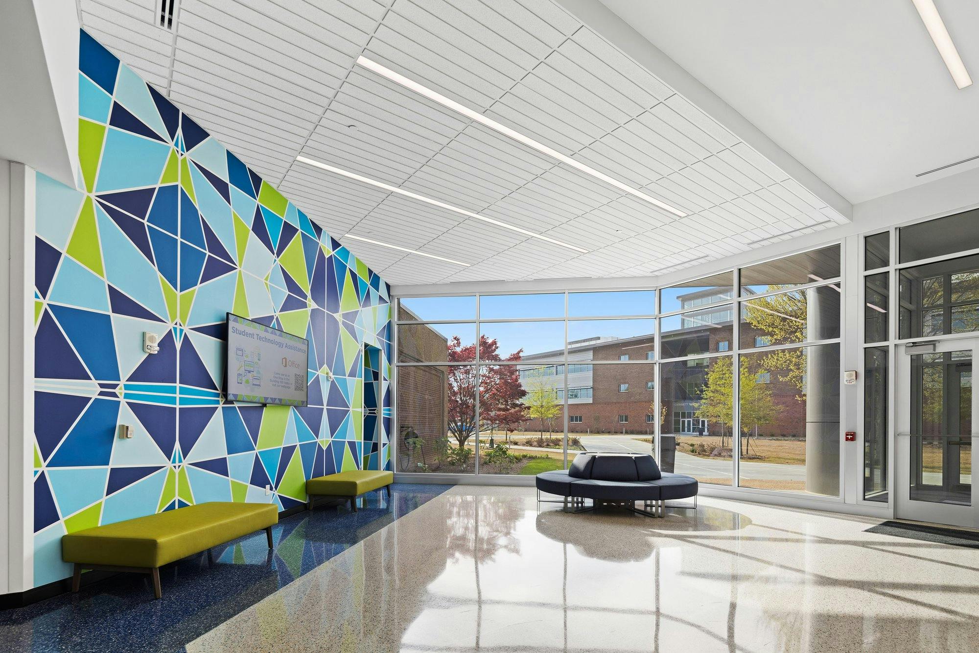 Glass-walled entryway with benches and way-finding TV screen on the wall.