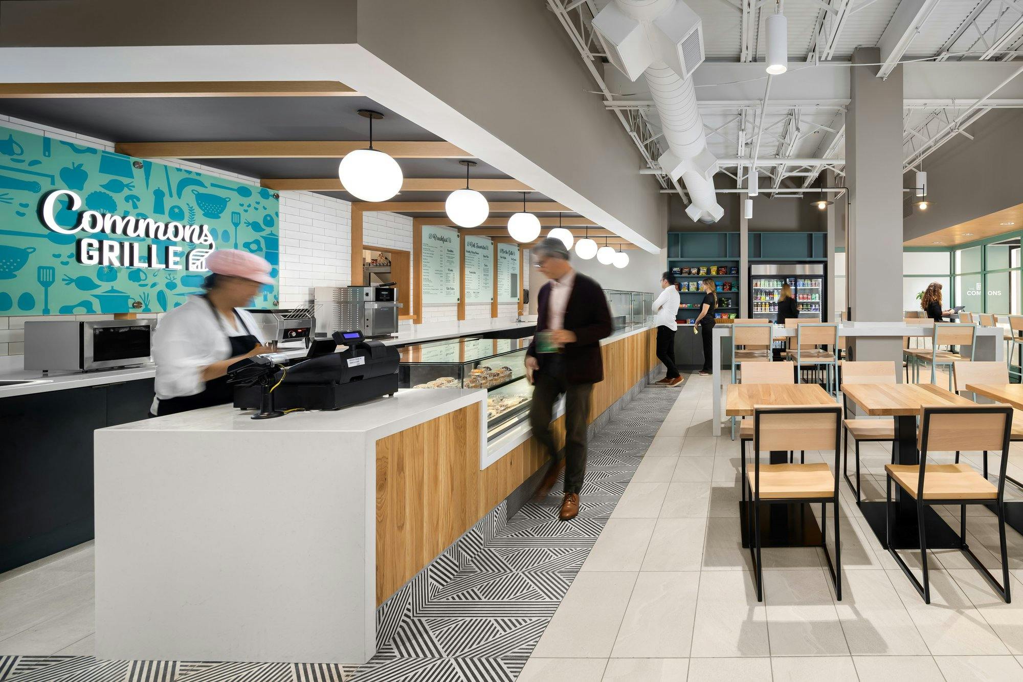 cafeteria in a commercial office building, with a cashier working in the foreground, and plenty of seating options 