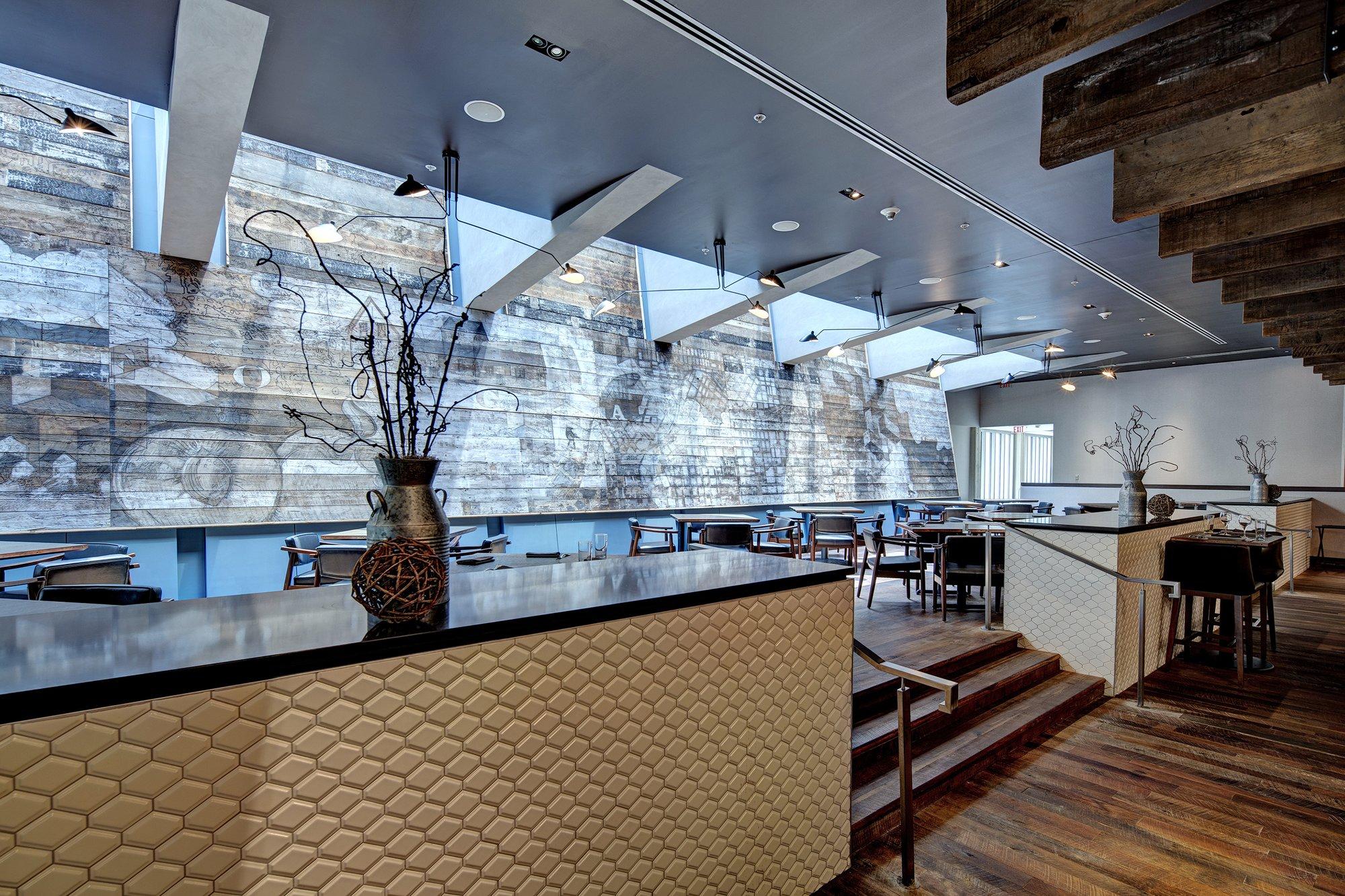 Restaurant floor with stairs leading to a seating area with a rustic modern wood wall.