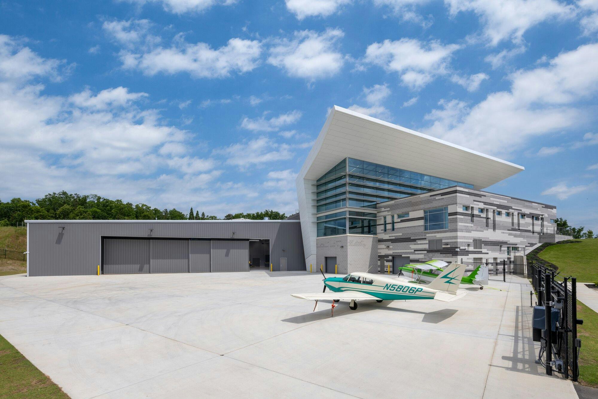 Exterior side view of building showcasing airplane hangar. Green airplane sitting out front.