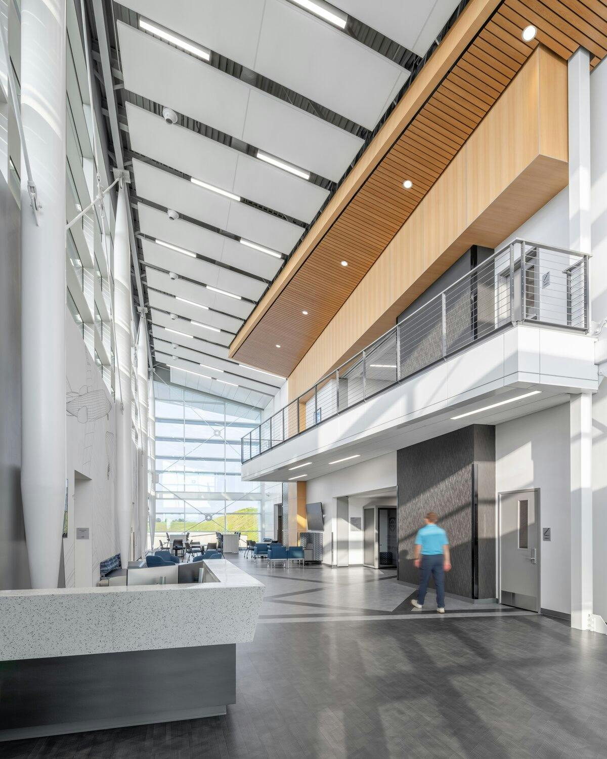 Interior lobby of building showing views of first and overhanging second floor. With a information desk and one wall of windows.