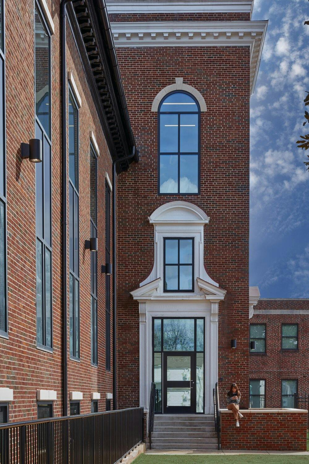 Exterior of the building leading up to stairs and a door with windows on every side with a detailed frame with two additional windows above the door.