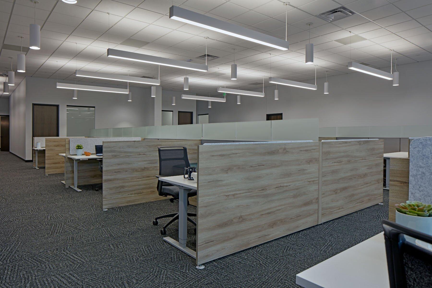 Office spaces with multiple desk and chairs, white walls and neutral colored carpet