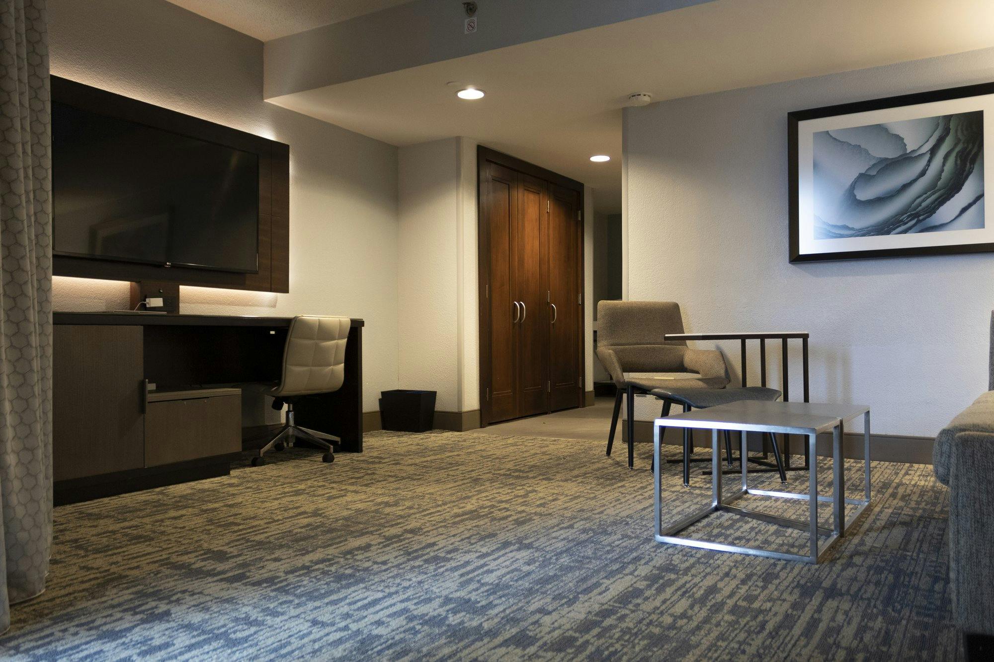 Hotel room seating area with chairs, tables, and TV mounted on the wall.