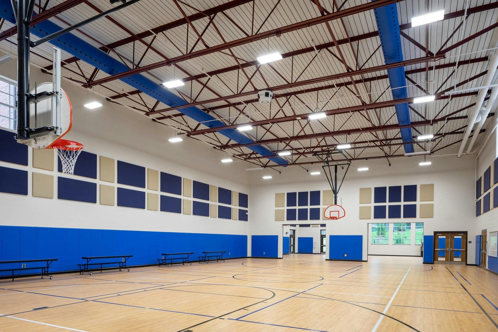 Basketball court in a gymnasium with high open ceilings and blue accents throughout.