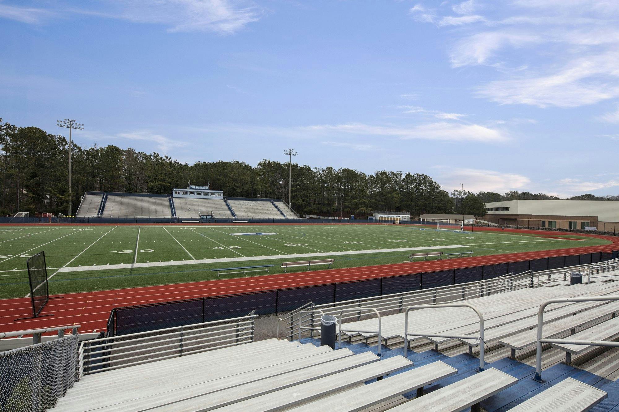 Metal bleachers leading down to a running track surrounding a grassy football field.