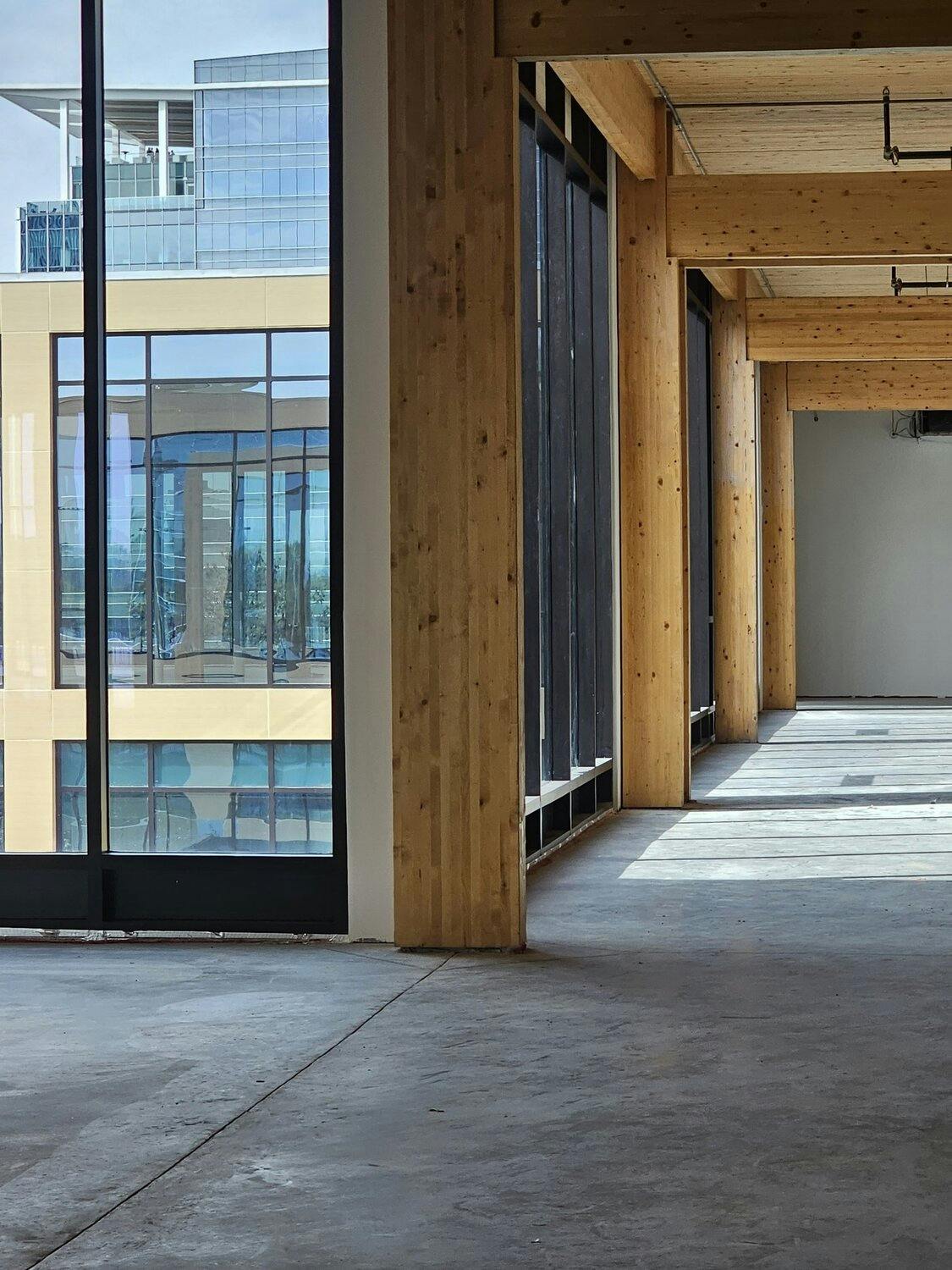 Hallway with cocrete floor, timber beams, and windows overlooking exterior of opposite side of building.