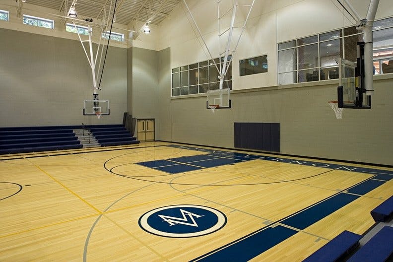 A crest with the letters "MV" painted on the floor of a gymnasium basketball court.