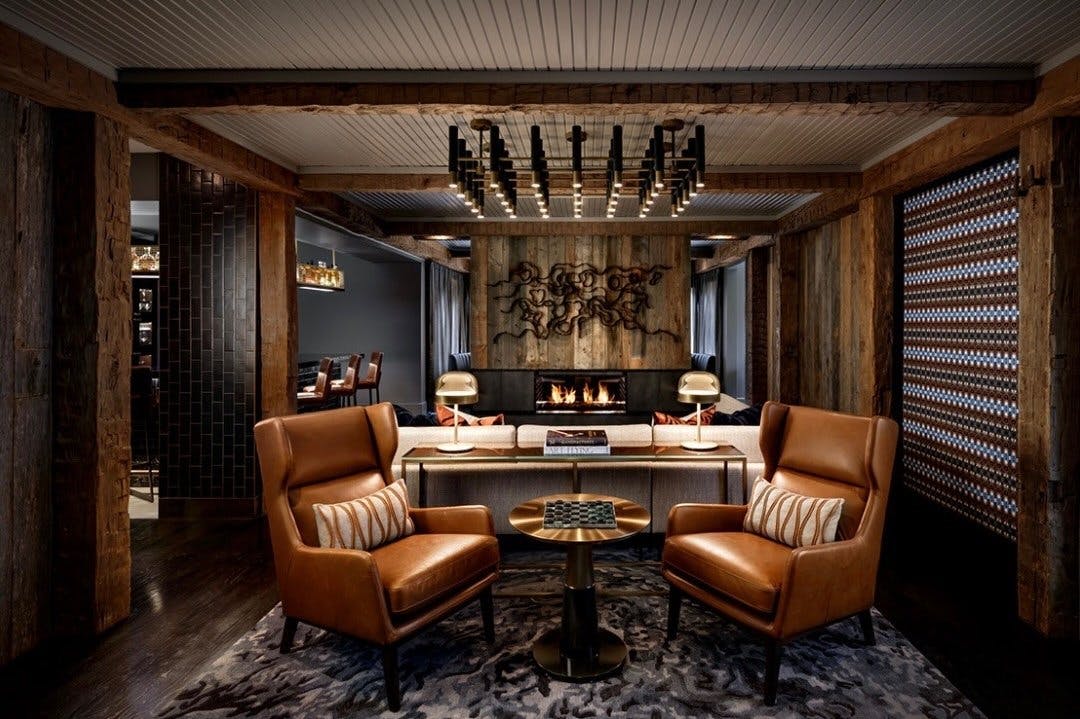 Two leather chairs in a lounge with dark features and a wood accent will containing a metal art piece.