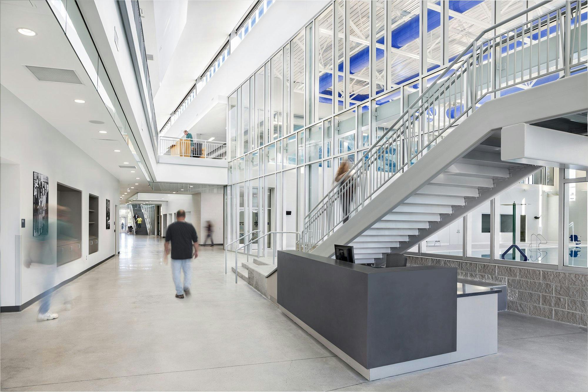 atrium of a recreation center showing a staircase leading to the second floor, artwork on the walls, and recreation rooms