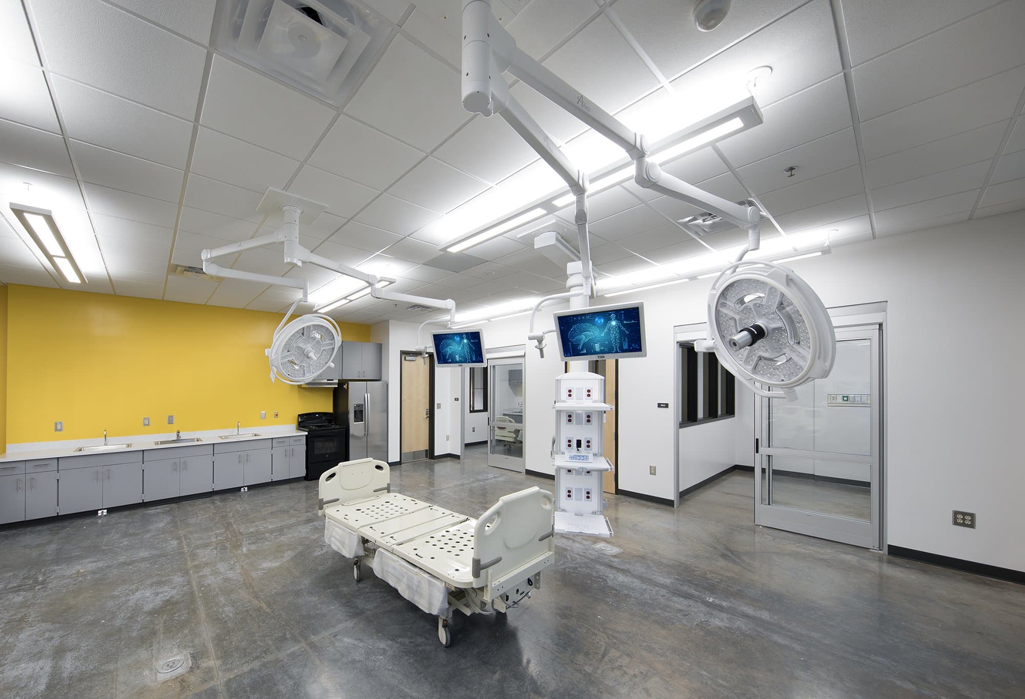 A medical education room with a hospital bed and multiple overhanging lights and screens.