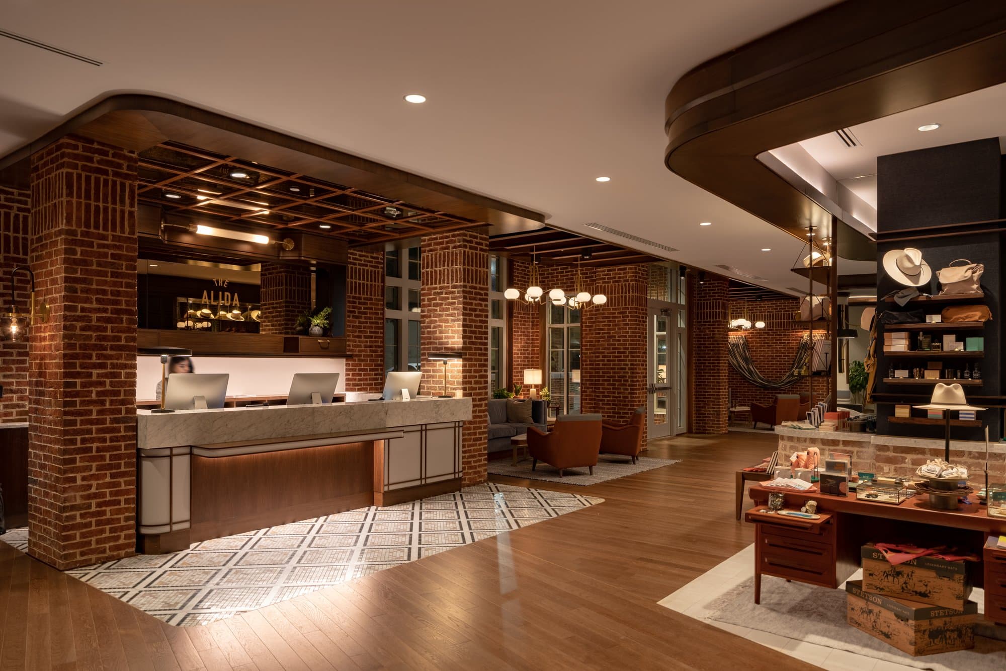 Reception area of The Alida Hotel with a mix of tile and wood floors throughout. A woman stands at a reception desk surrounded by brick columns.