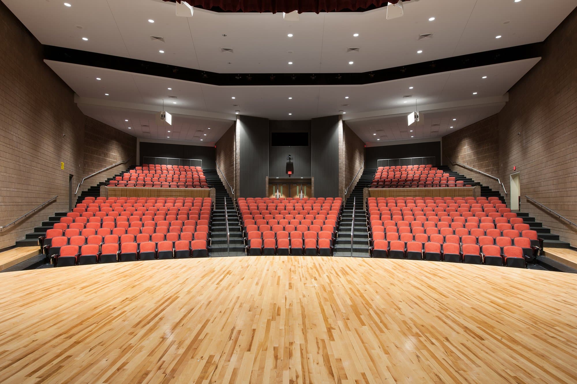 Rows of red seats can be seen from the stage of a wide open auditorium.
