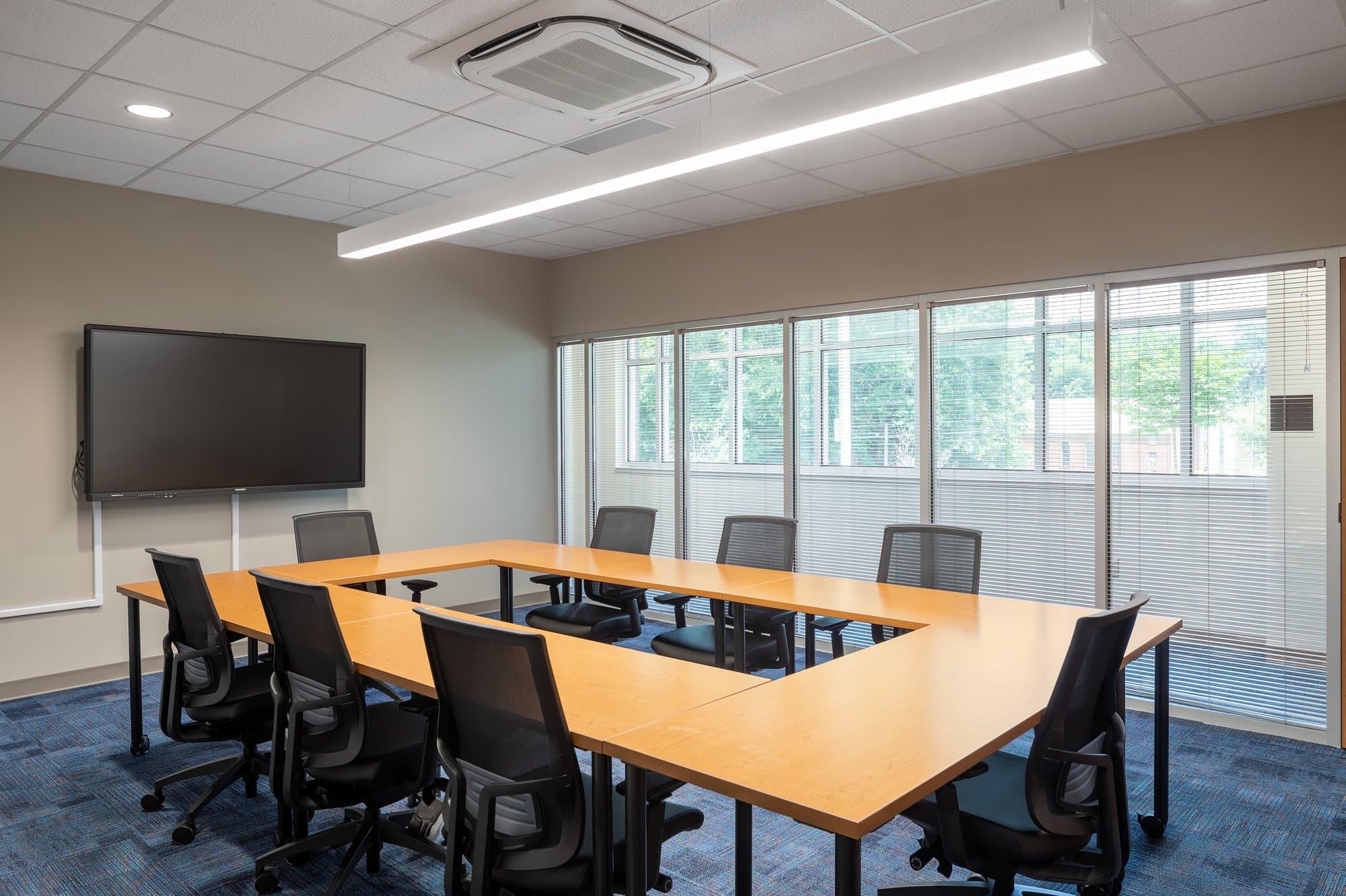 Tables and office chairs arranged in an open rectangle comprise the floor space of a conference room.