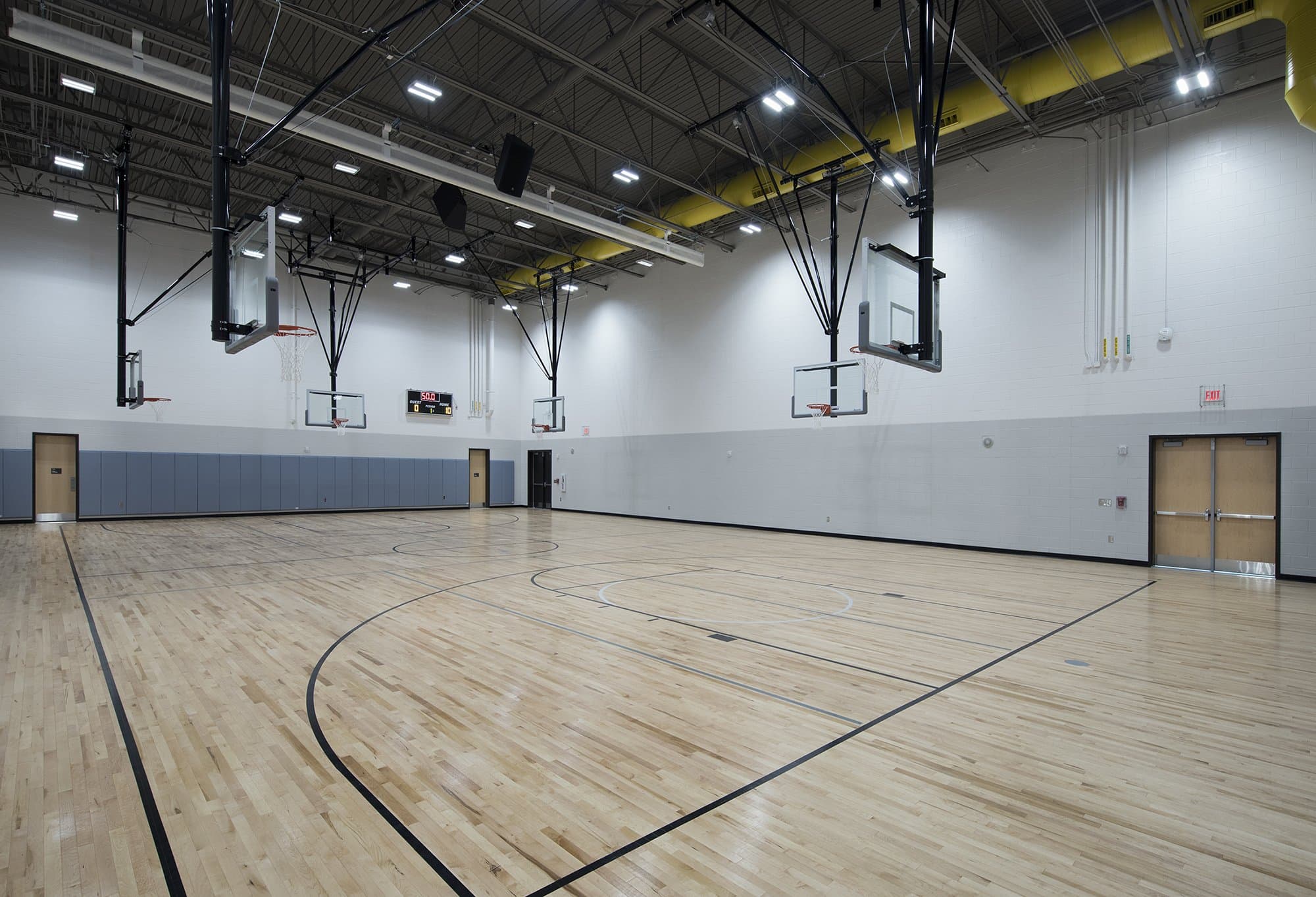 A gymnasium basketball court with light stained wood floors and black painted lines.