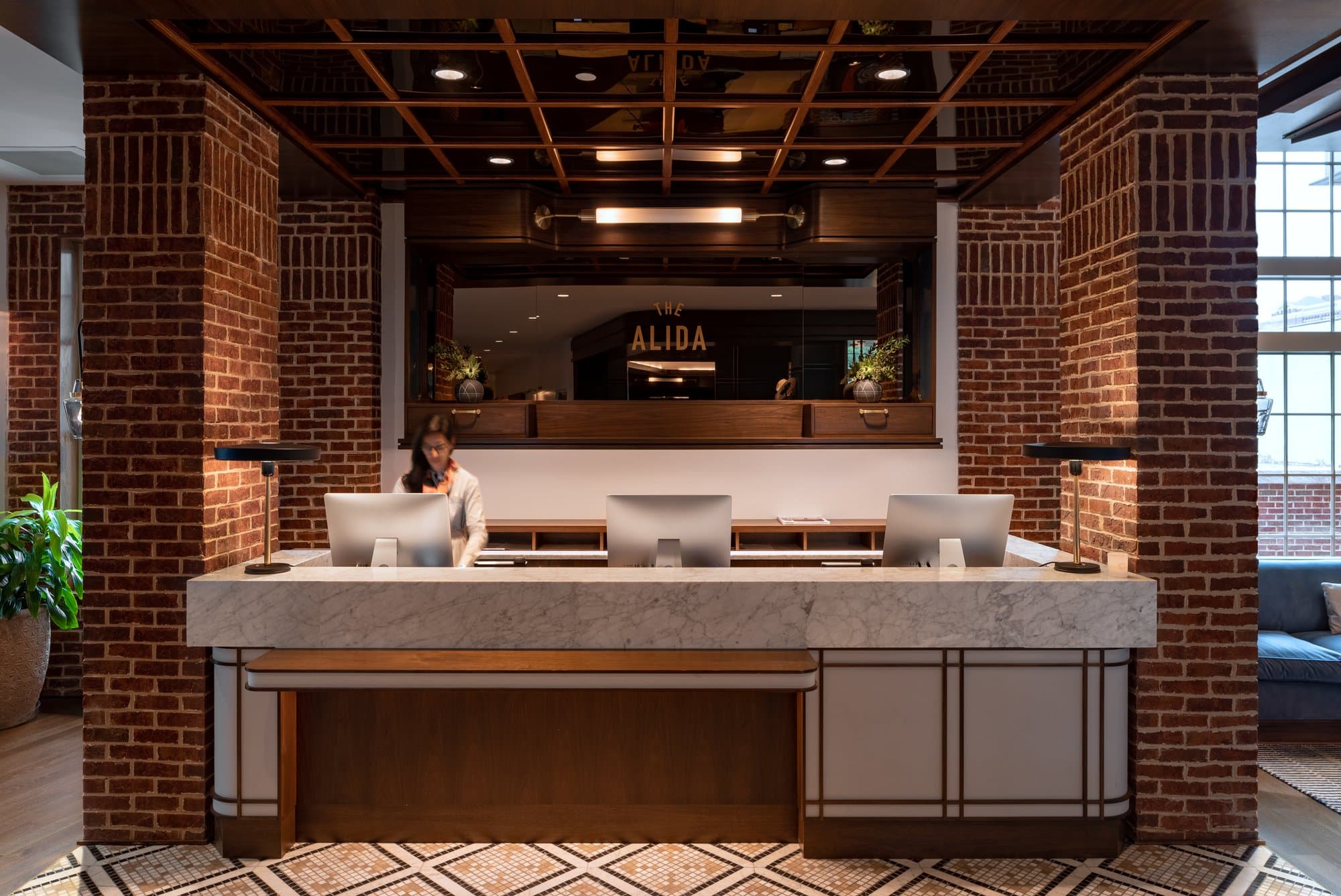 Woman stands in front of a computer at a marble reception desk surrounded by brick columns.