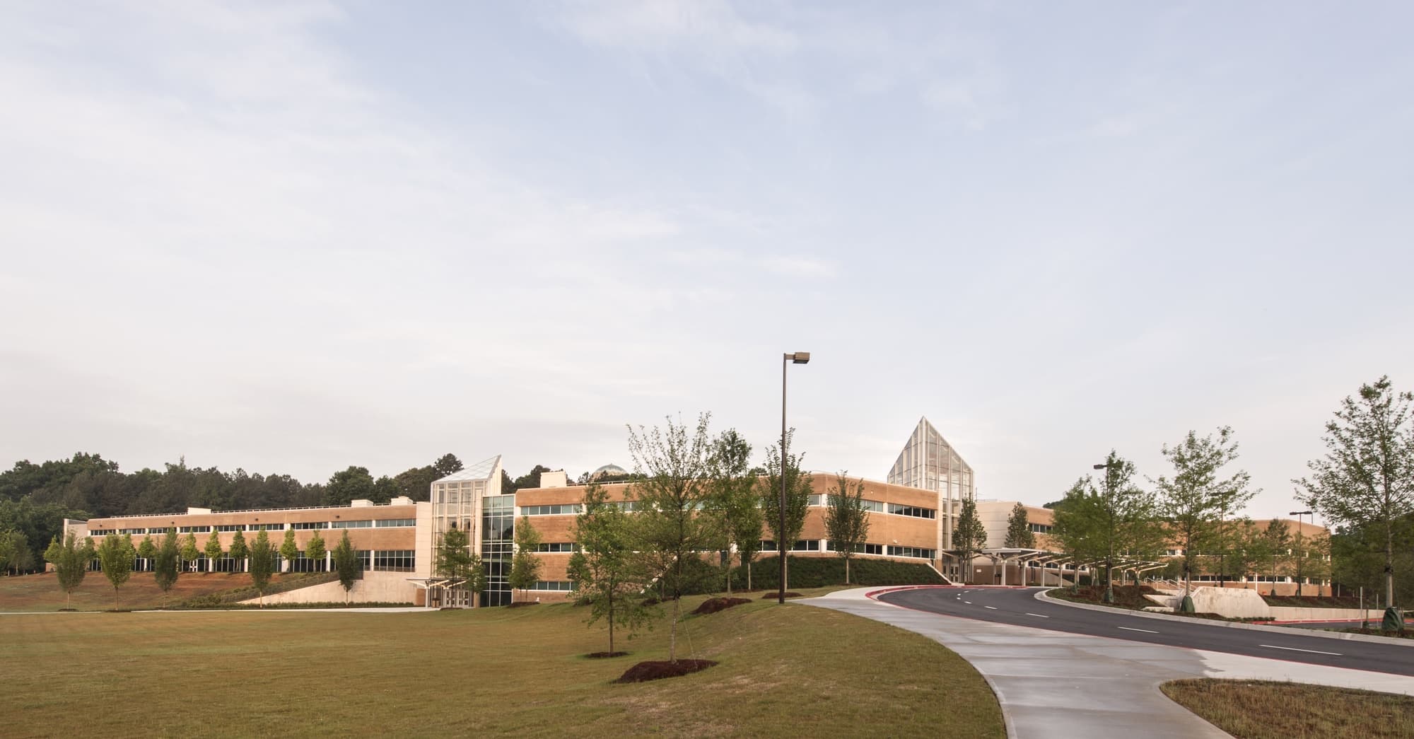 Complete outside view of school. Heavy brick with windows, grassy hill and parking.